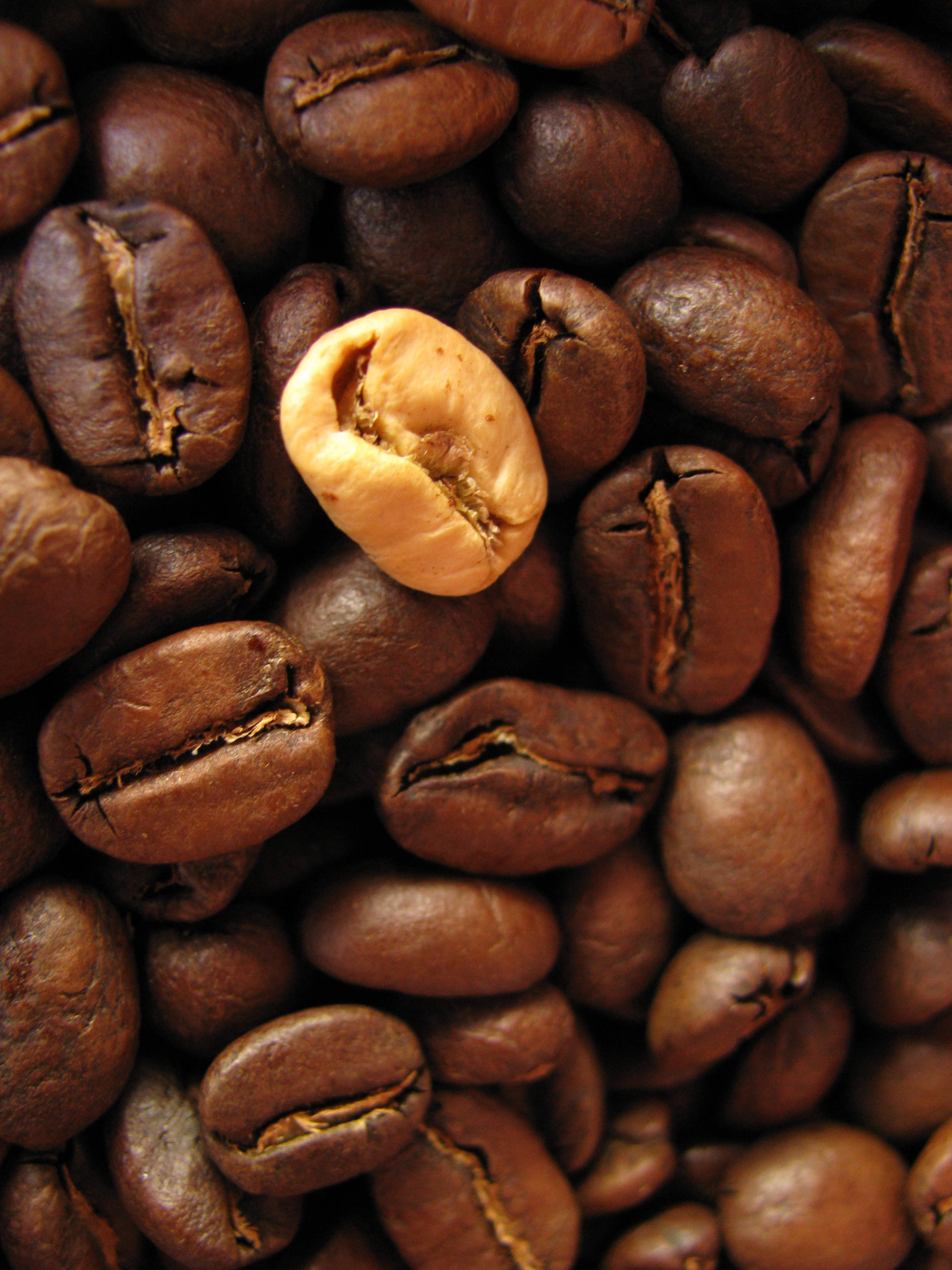 beans 桌布 壁紙 — 烘焙咖啡豆的特寫，其中一顆裂開，露出淡色的內部種子。
