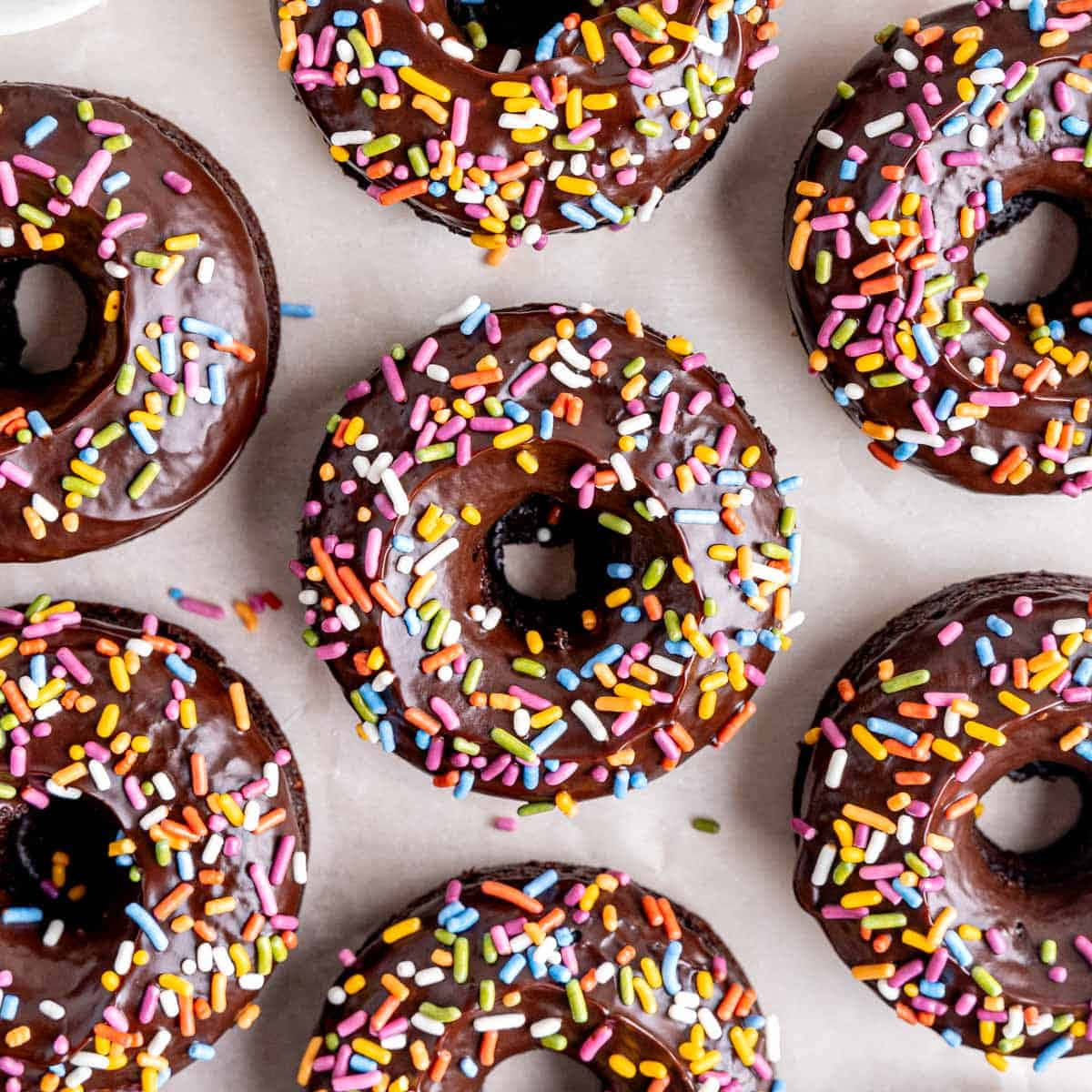 Donut 桌布 壁紙 — 烘焙紙上巧克力釉面甜甜圈撒上彩色糖粒的俯瞰照片。