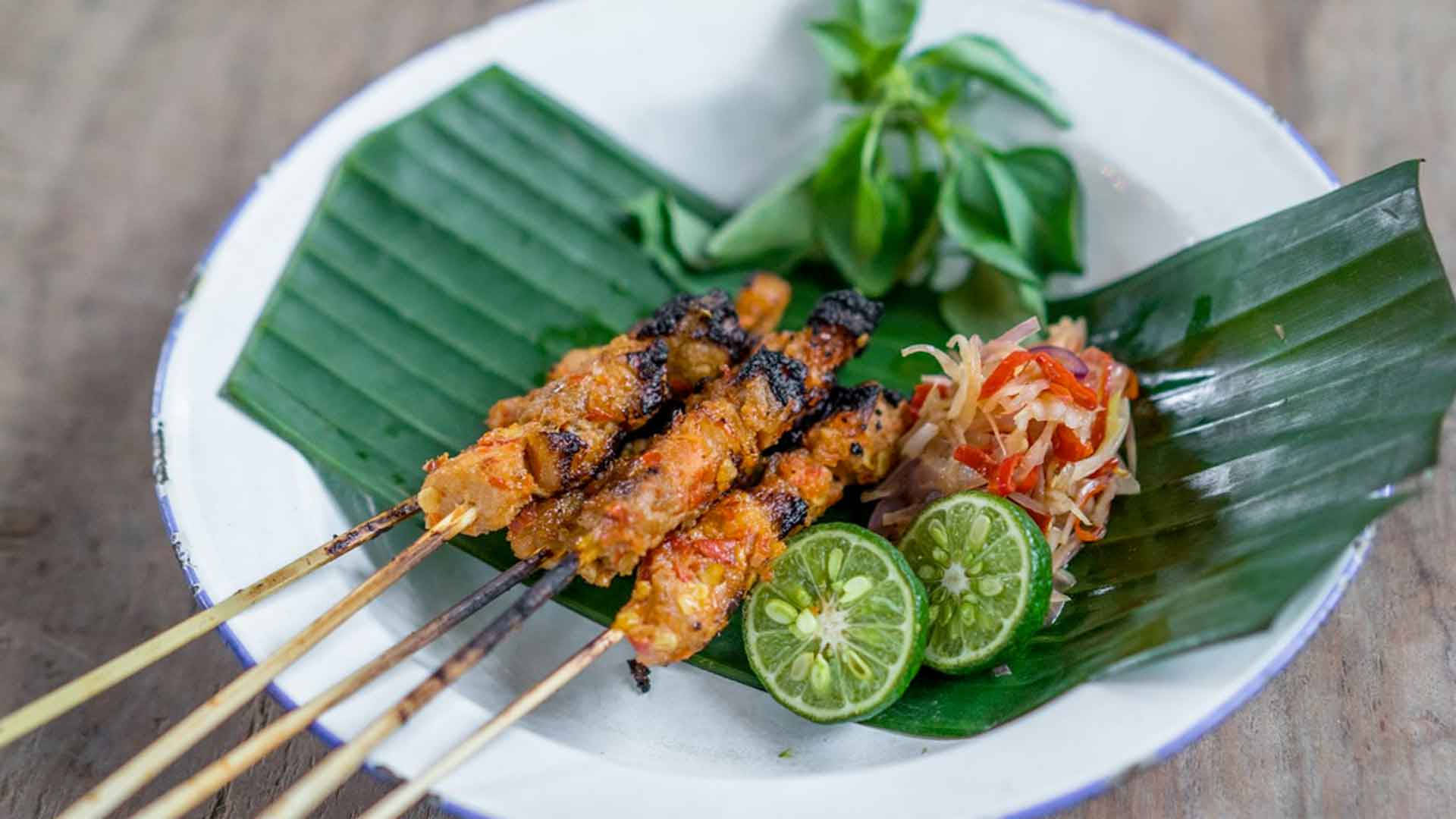 Delicious Food 桌布 壁紙 — 烤沙嗲串燒配焦肉和新鮮萊姆片，放在白色盤子上的香蕉葉上。
