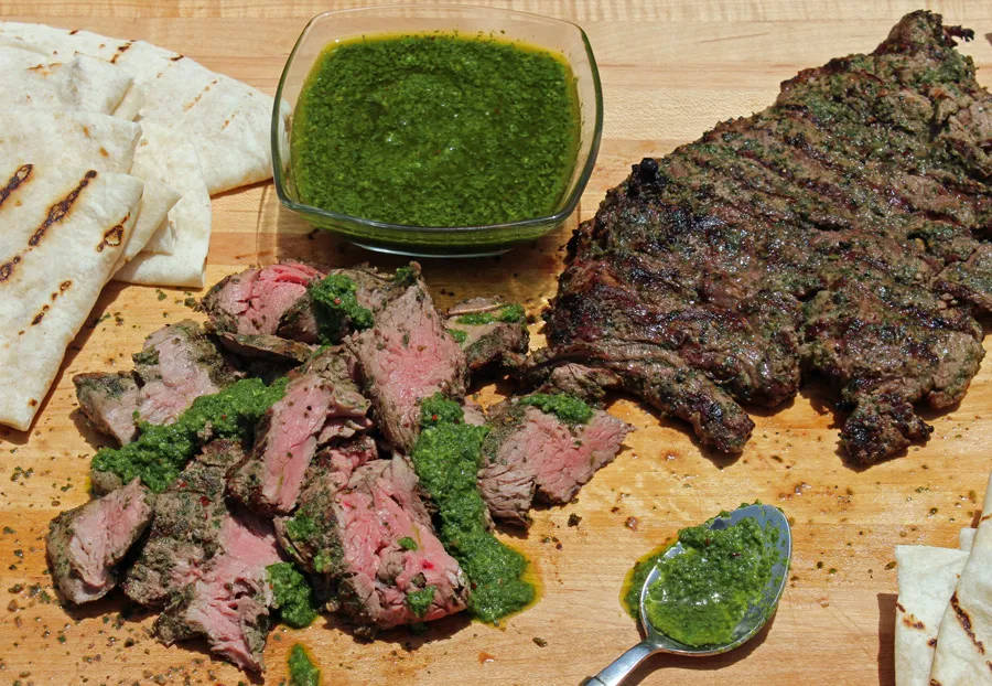 meat 桌布 壁紙 — 烤牛排切片搭配阿根廷青醬，置於木板上，附有玉米餅和湯匙。