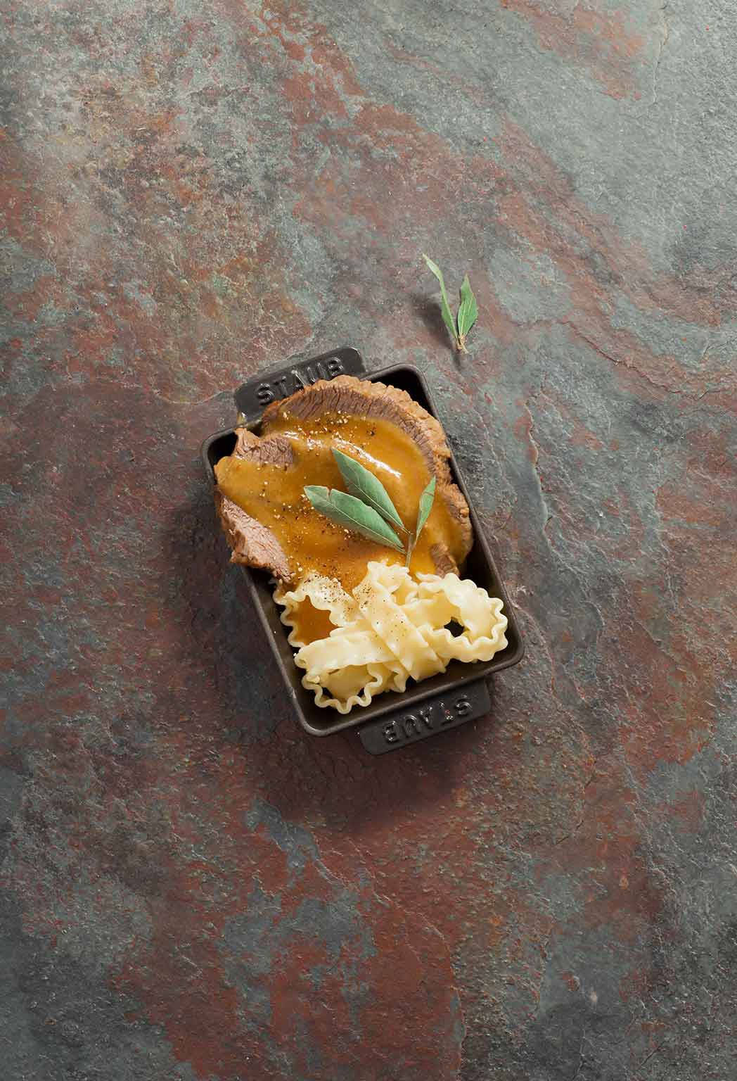 meat 桌布 壁紙 — 烤牛里脊肉配濃郁肉汁和皺邊義大利麵，盛載於黑色STAUB鍋中，置於紋理鏽蝕金屬表面上。