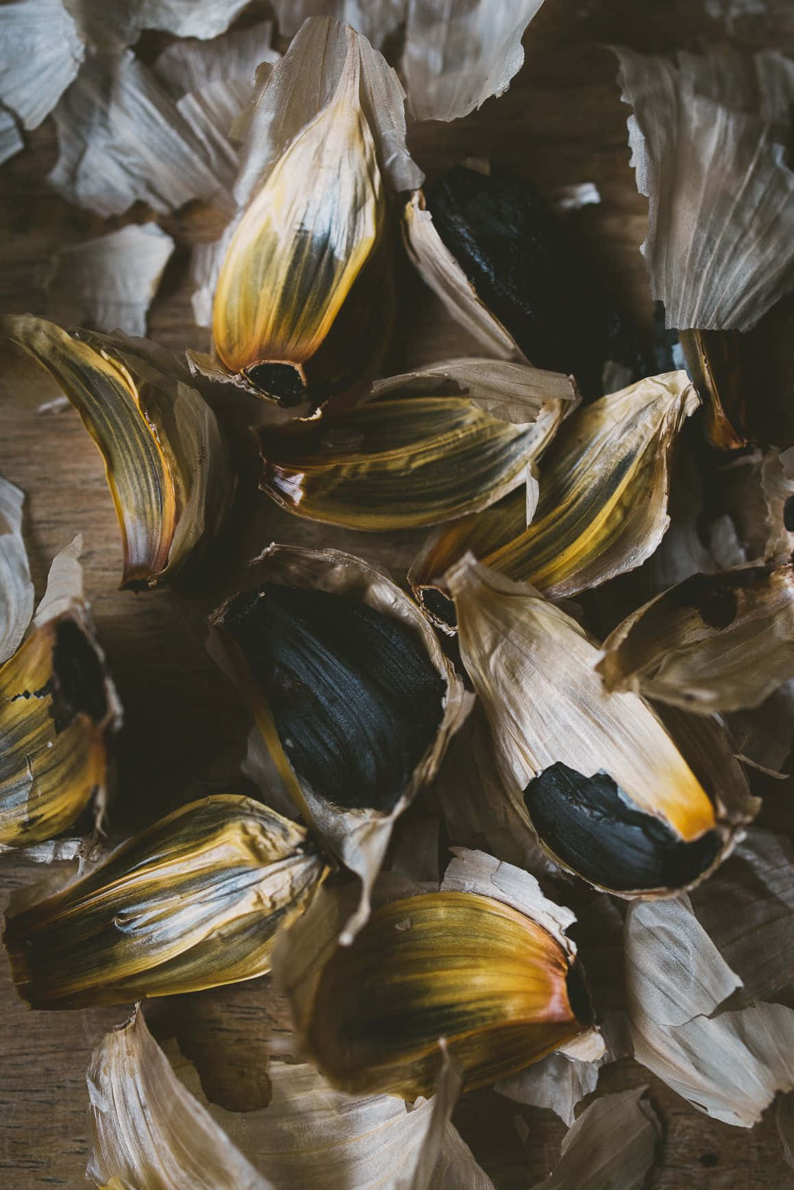 Black Garlic 桌布 壁紙 — 烤蒜瓣的特寫，帶有燒焦的尖端和薄皮，散落在木質表面上。