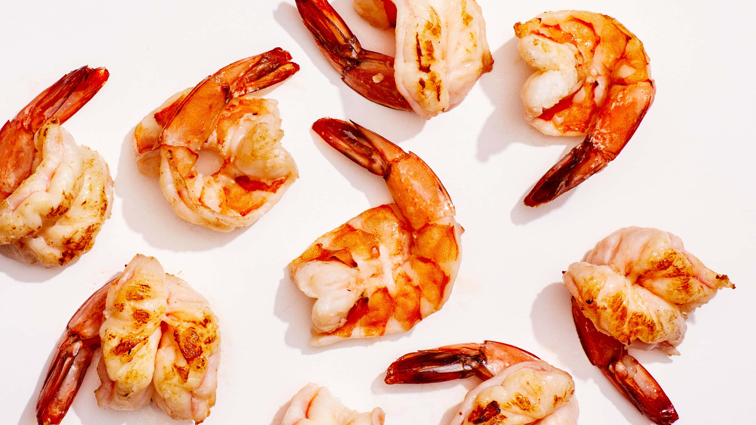 shrimp 桌布 壁紙 — 烤蝦帶有焦糖尾巴，散落在明亮白色表面上，柔和燈光下。