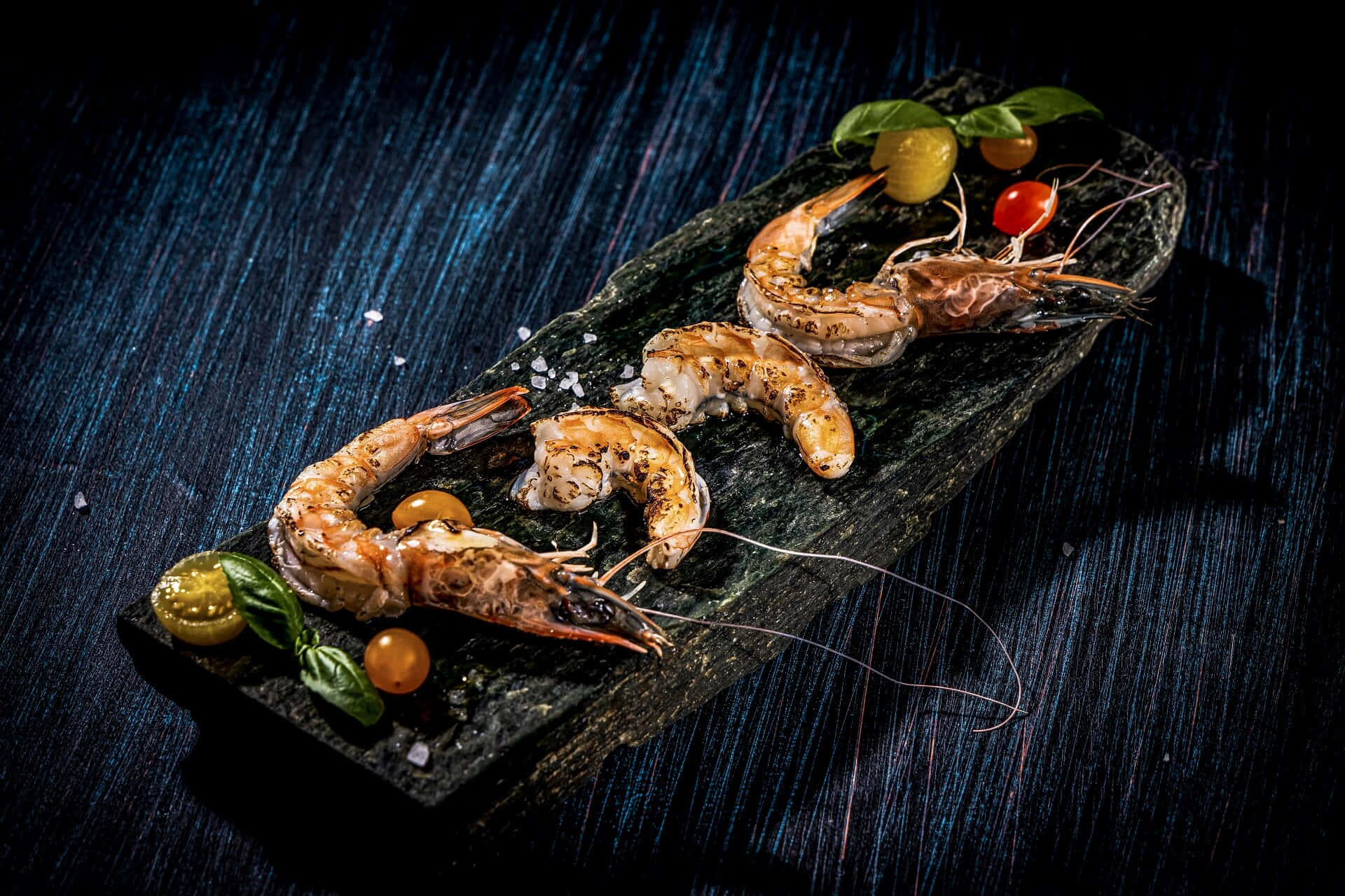 shrimp 桌布 壁紙 — 烤蝦配羅勒和櫻桃番茄，放在深色石板上，背景為有紋理的藍色。
