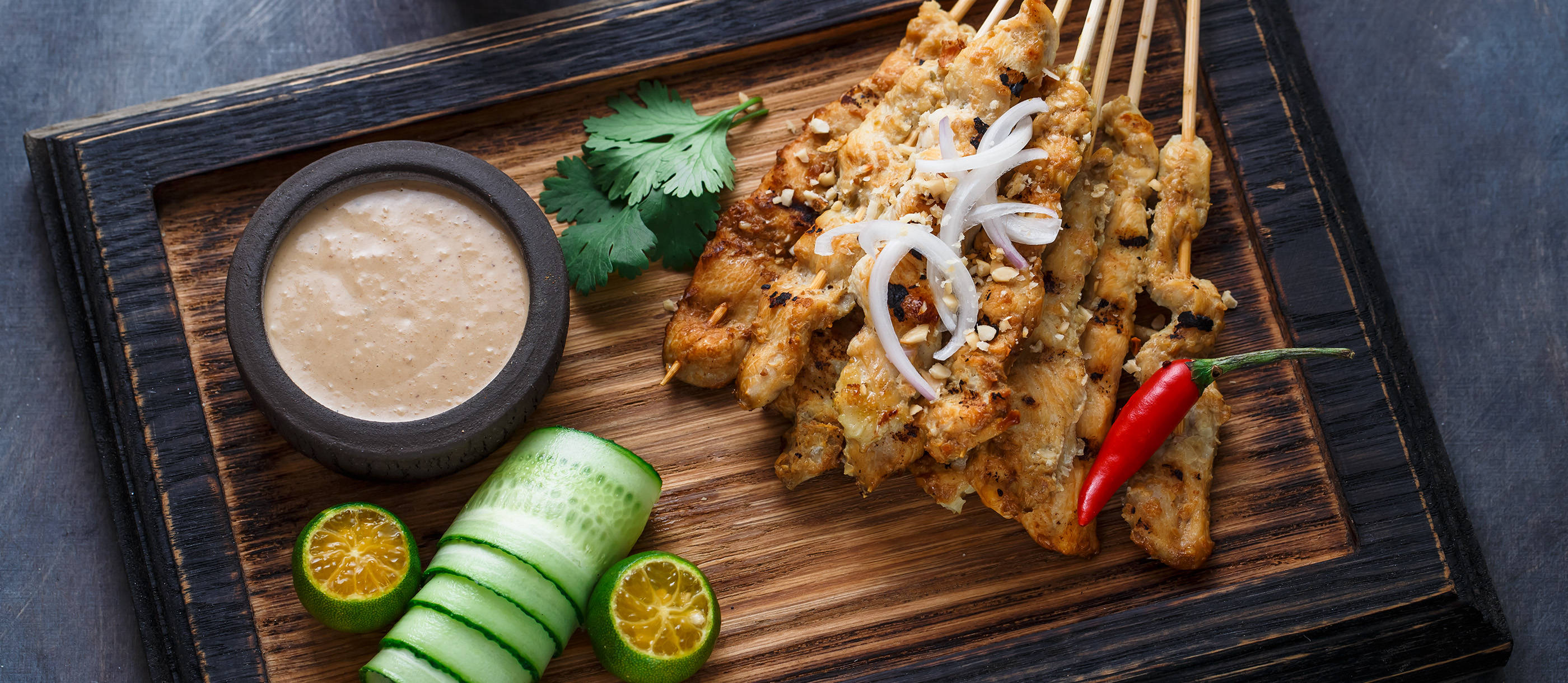 Food Photography 桌布 壁紙 — 烤雞肉沙爹串，飾以洋蔥、香菜和辣椒，配上花生醬、小黃瓜和萊姆，放在木板上。