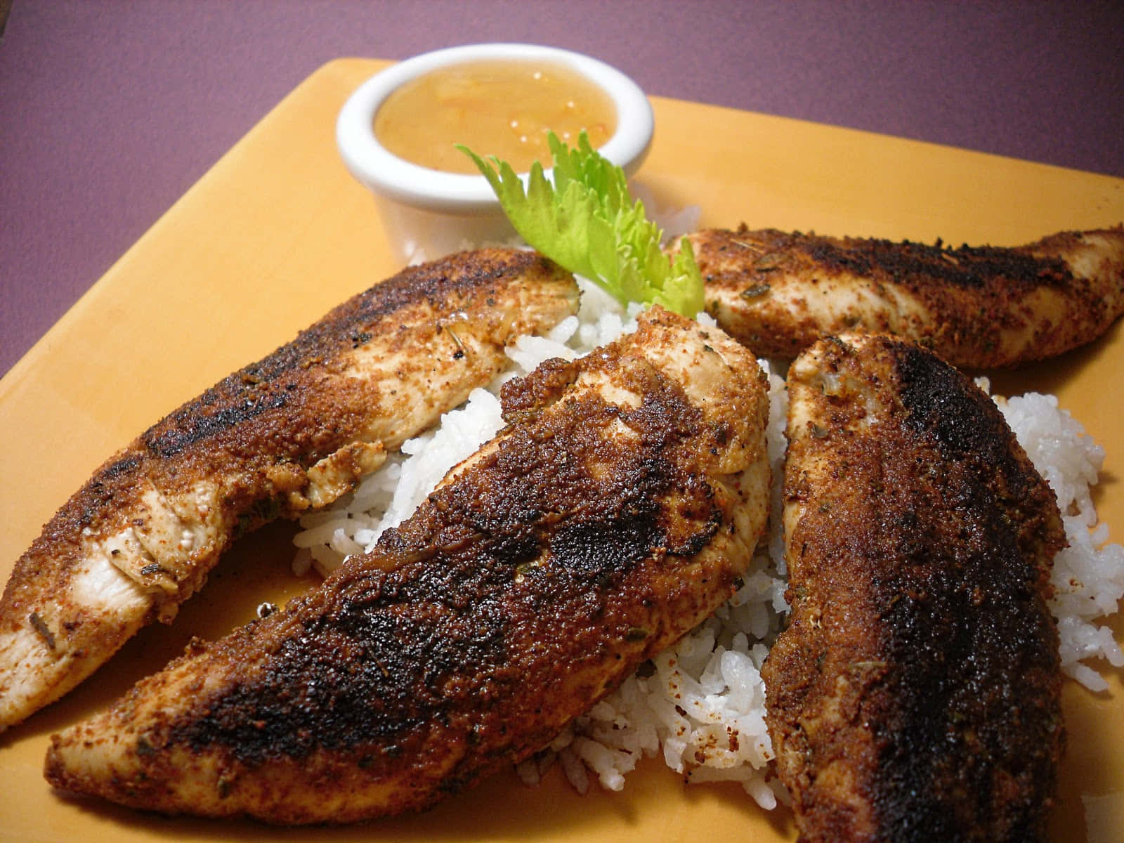 Blackened Chicken 桌布 壁紙 — 烤雞胸肉搭配焦香香料，放在白飯上，置於黃色盤中，附上蘸醬和新鮮生菜。