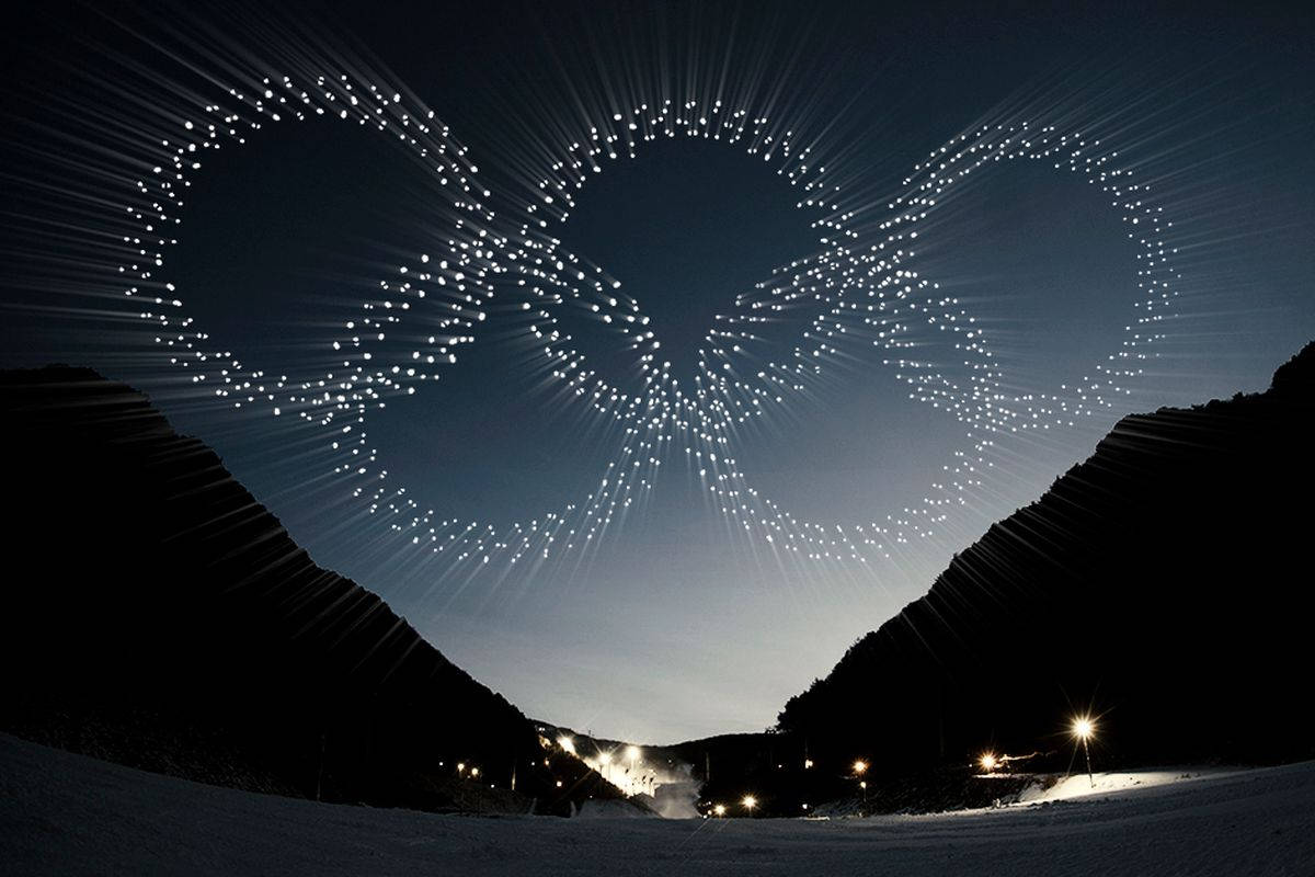 Winter Olympics 桌布 壁紙 — 無人機在暮色天空下，於黑暗的山谷中形成發光的奧運五環。