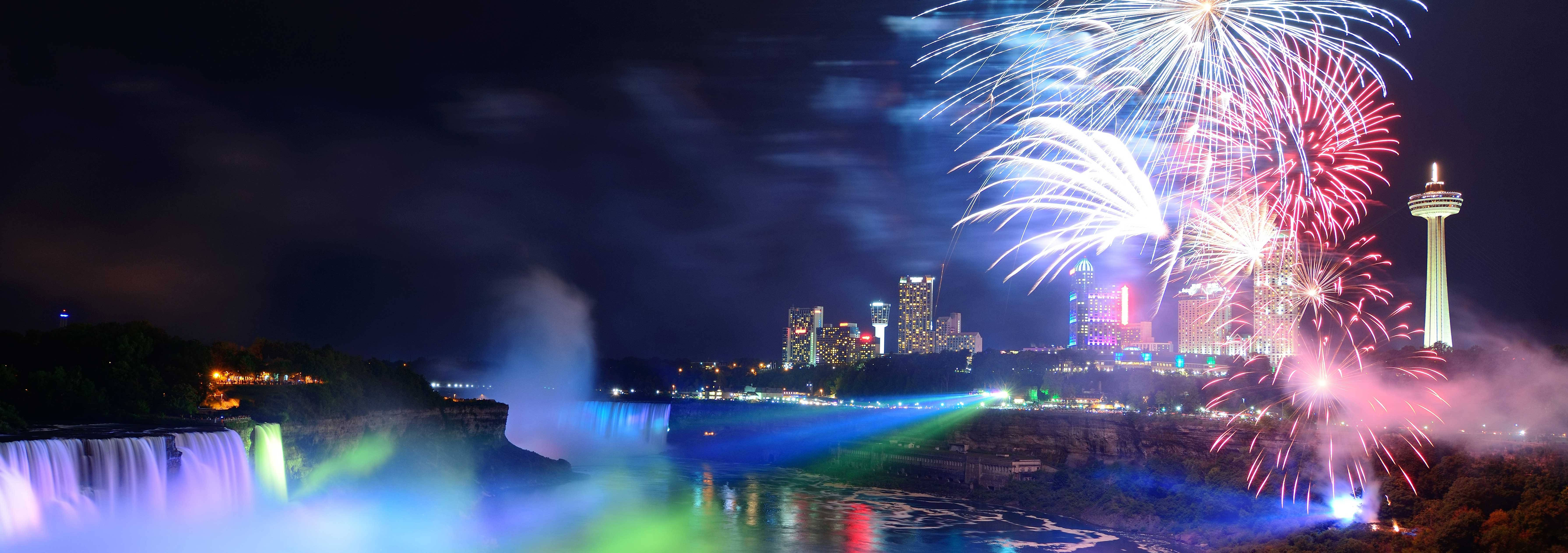 niagara 桌布 壁紙 — 煙火在夜間於尼亞加拉大瀑布上空爆炸，以鮮豔的色彩照亮霧氣和城市天際線。