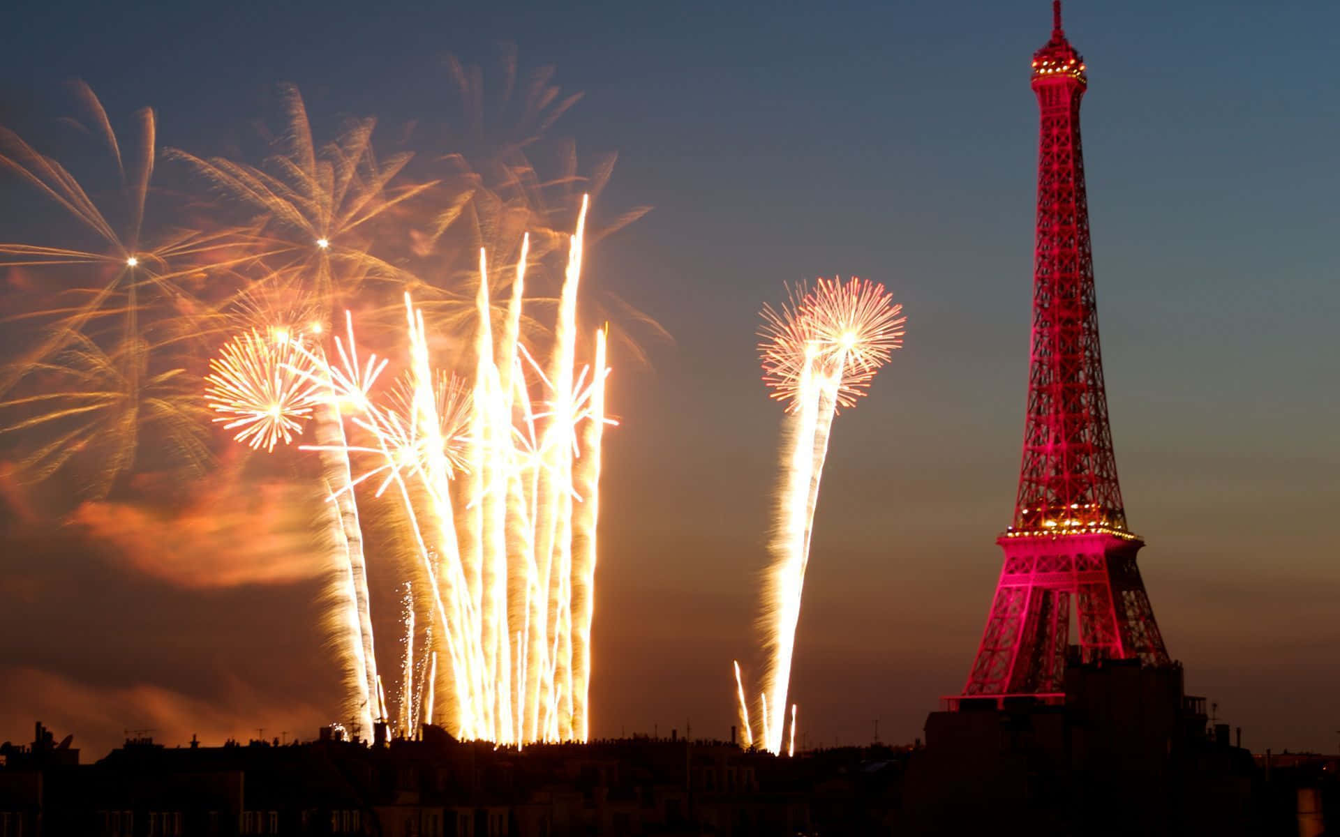 Paris Desktop 桌布 壁紙 — 煙火在巴黎上空金色綻放，艾菲爾鐵塔在暮色天空下閃耀粉紅光芒。