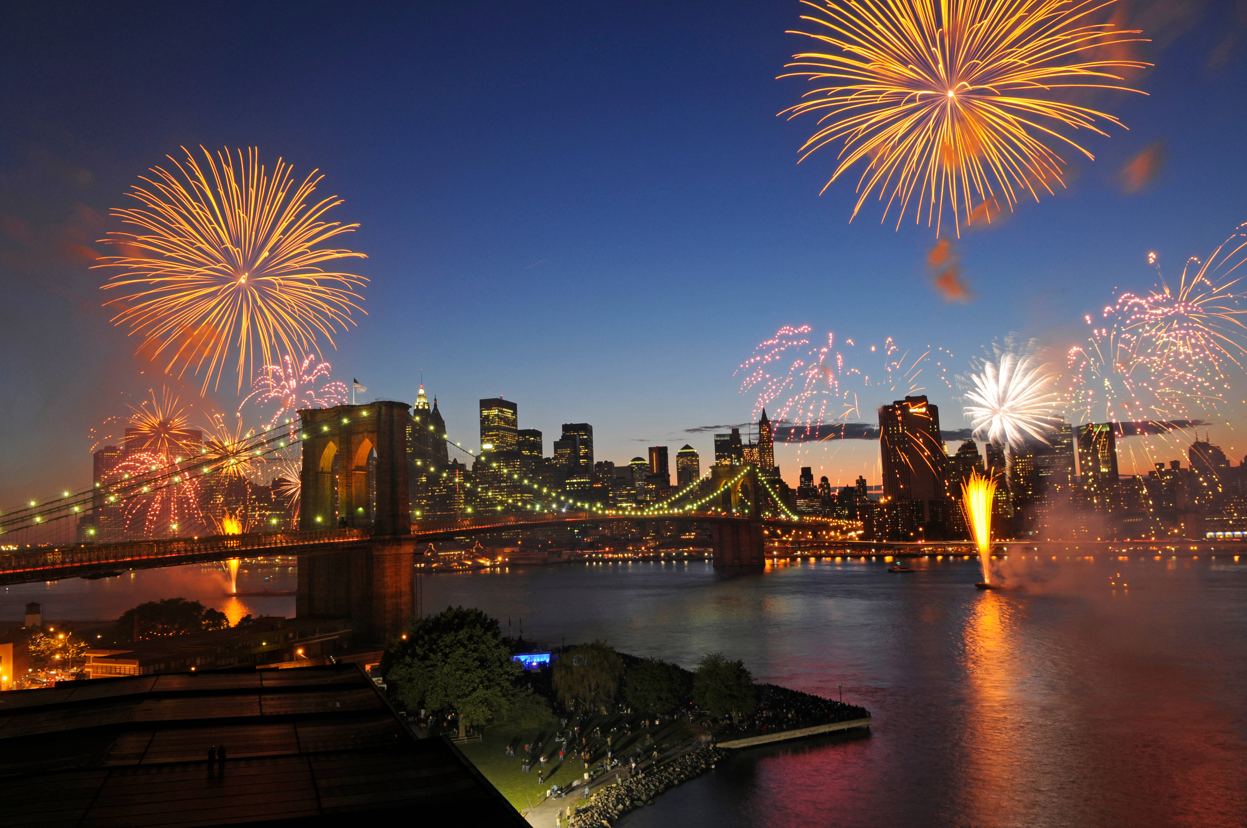 Fireworks 桌布 壁紙 — 煙火在布魯克林大橋和曼哈頓天際線上空於黃昏時爆炸，倒映在水面上。
