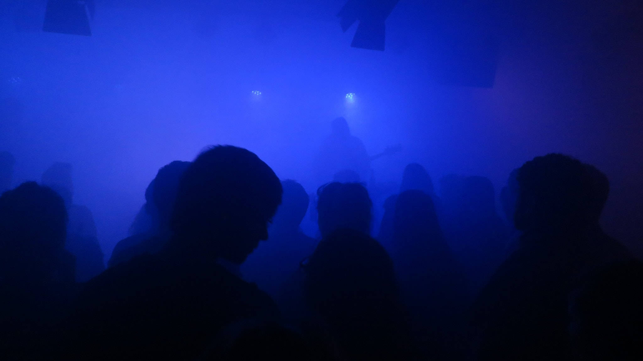 人物 桌布 壁紙 — 煙霧瀰漫的夜店中，人們的剪影沐浴在強烈的藍色舞台燈光下。