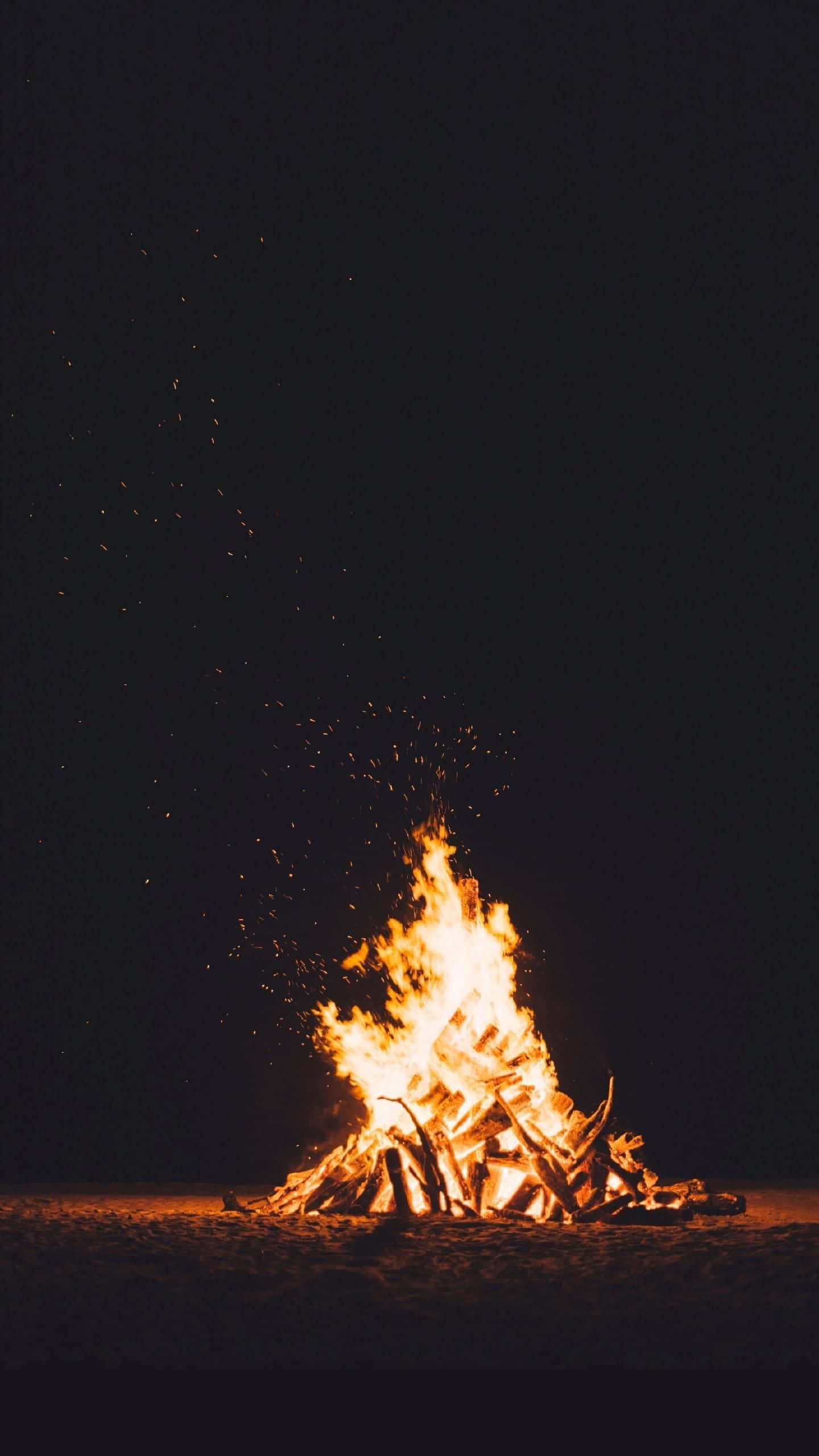 LED 桌布 壁紙 — 熊熊營火在夜間明亮燃燒，向黑暗的天空投射溫暖的光芒和火花。