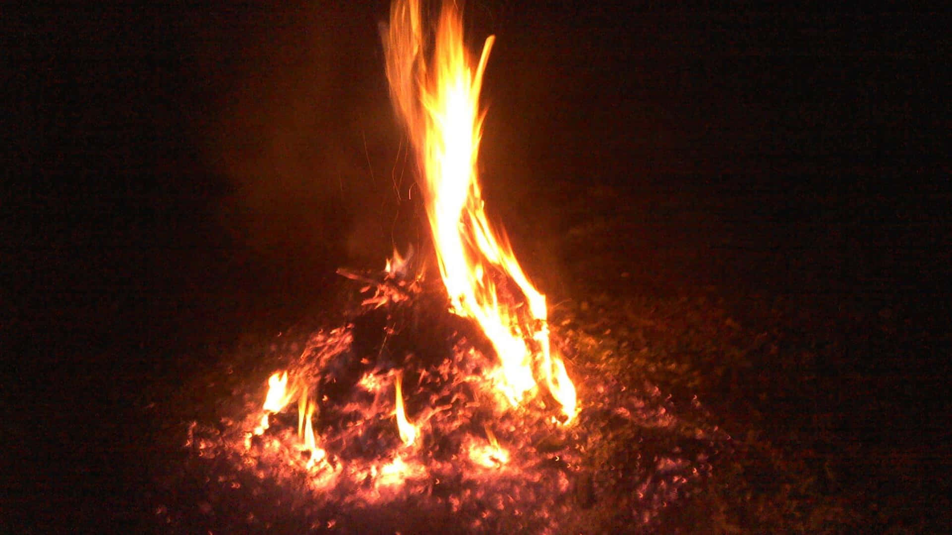 Campfire 桌布 壁紙 — 熊熊營火在漆黑的夜空下明亮燃燒，向周圍地面投射溫暖的橙色光芒。
