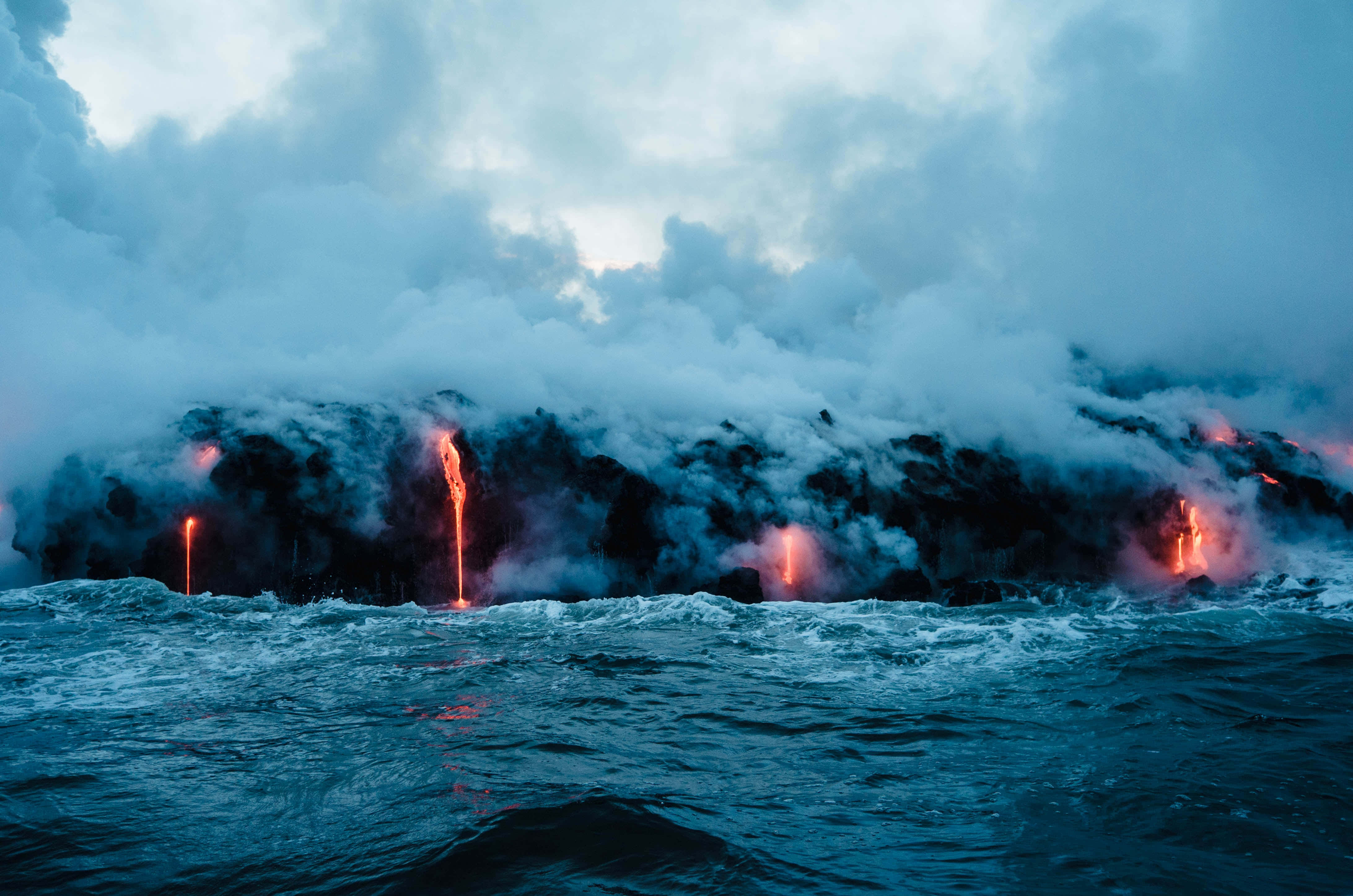 Aesthetic Hawaii 桌布 壁紙 — 熔岩流從火山海岸線噴湧入海，在多雲的天空下形成蒸汽羽流。