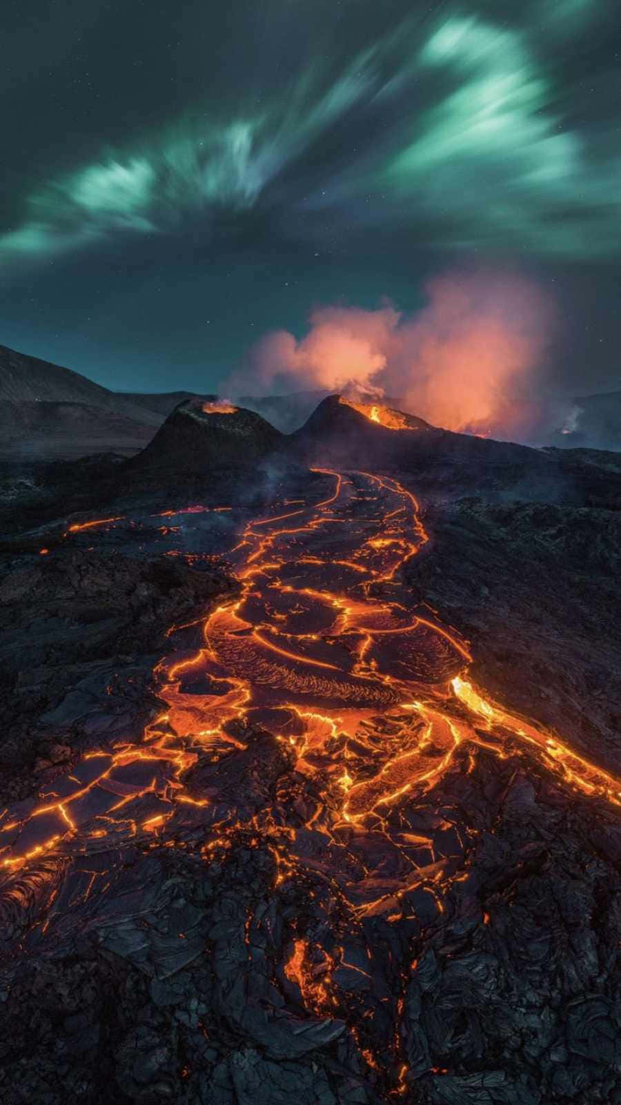 Volcano 桌布 壁紙 — 熔岩流發出火熱的橙色光芒，在星空和綠色極光下沿著火山山脈傾瀉而下。