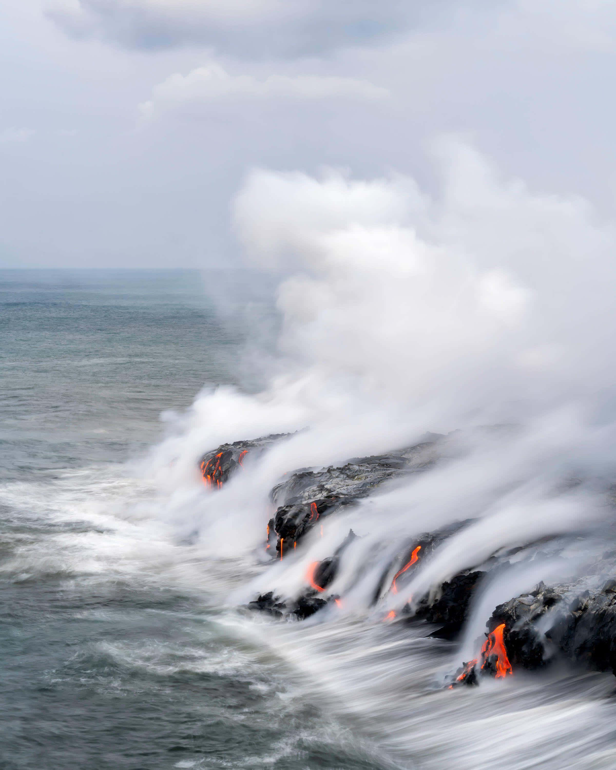 Volcano 桌布 壁紙 — 熔岩流與海浪相遇，在黑色岩石上形成翻滾的蒸氣和發光的橙色裂縫。