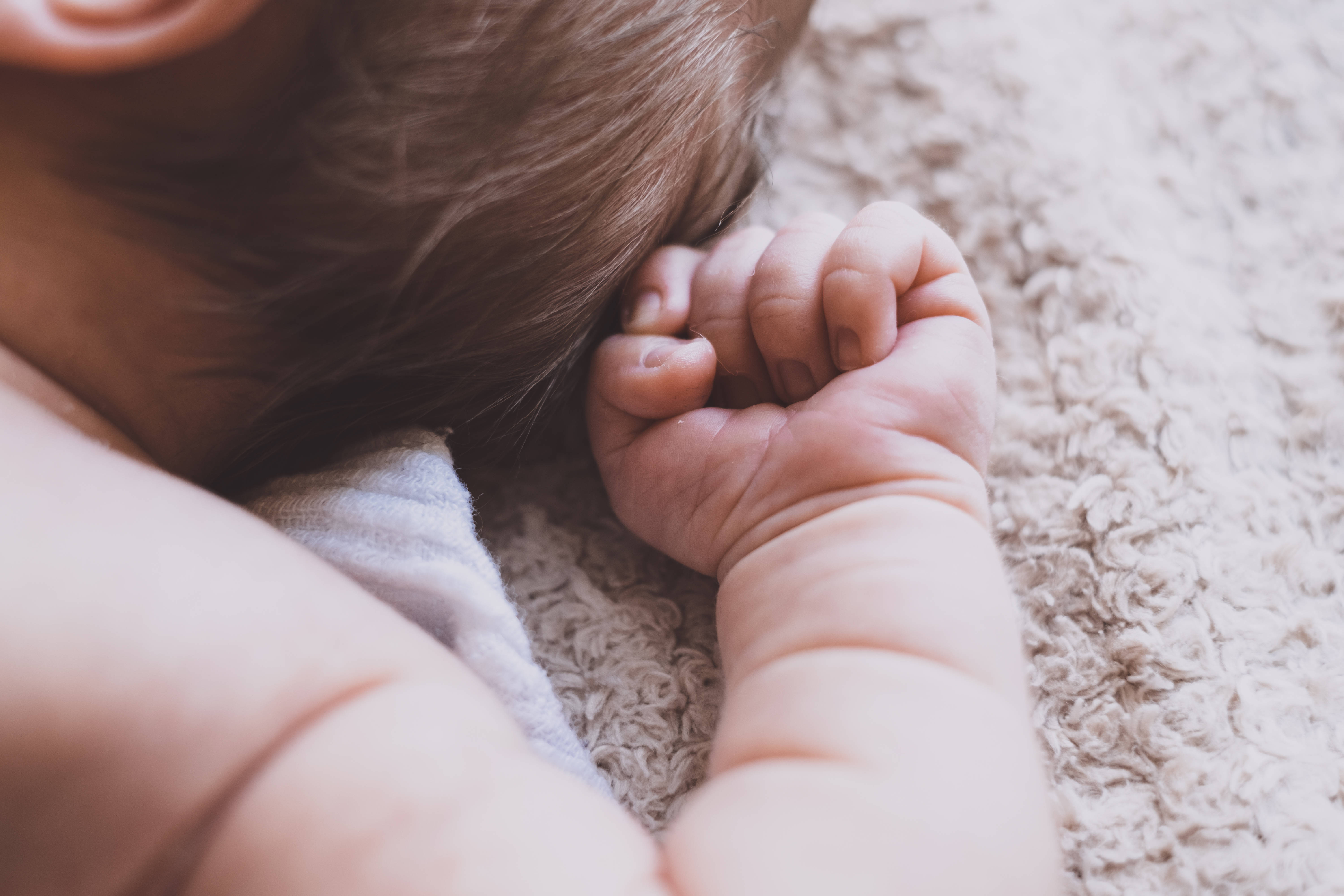 Baby Boy 桌布 壁紙 — 熟睡嬰兒頭部和緊握的小拳頭的特寫，放在柔軟的米色地毯上。