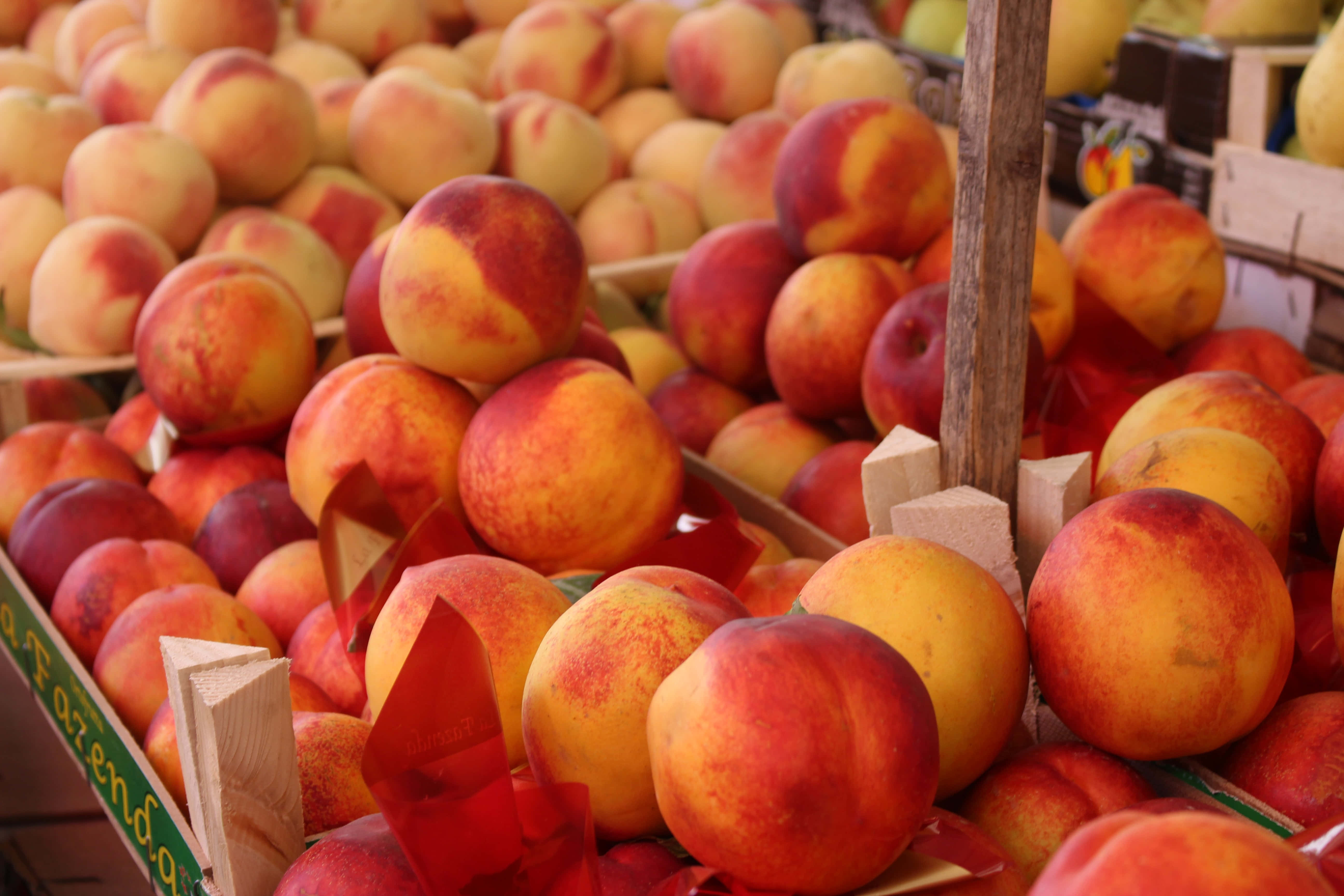 Peaches 桌布 壁紙 — 熟透的桃子高高堆放在木箱中，在熙攘的戶外市場攤位上。