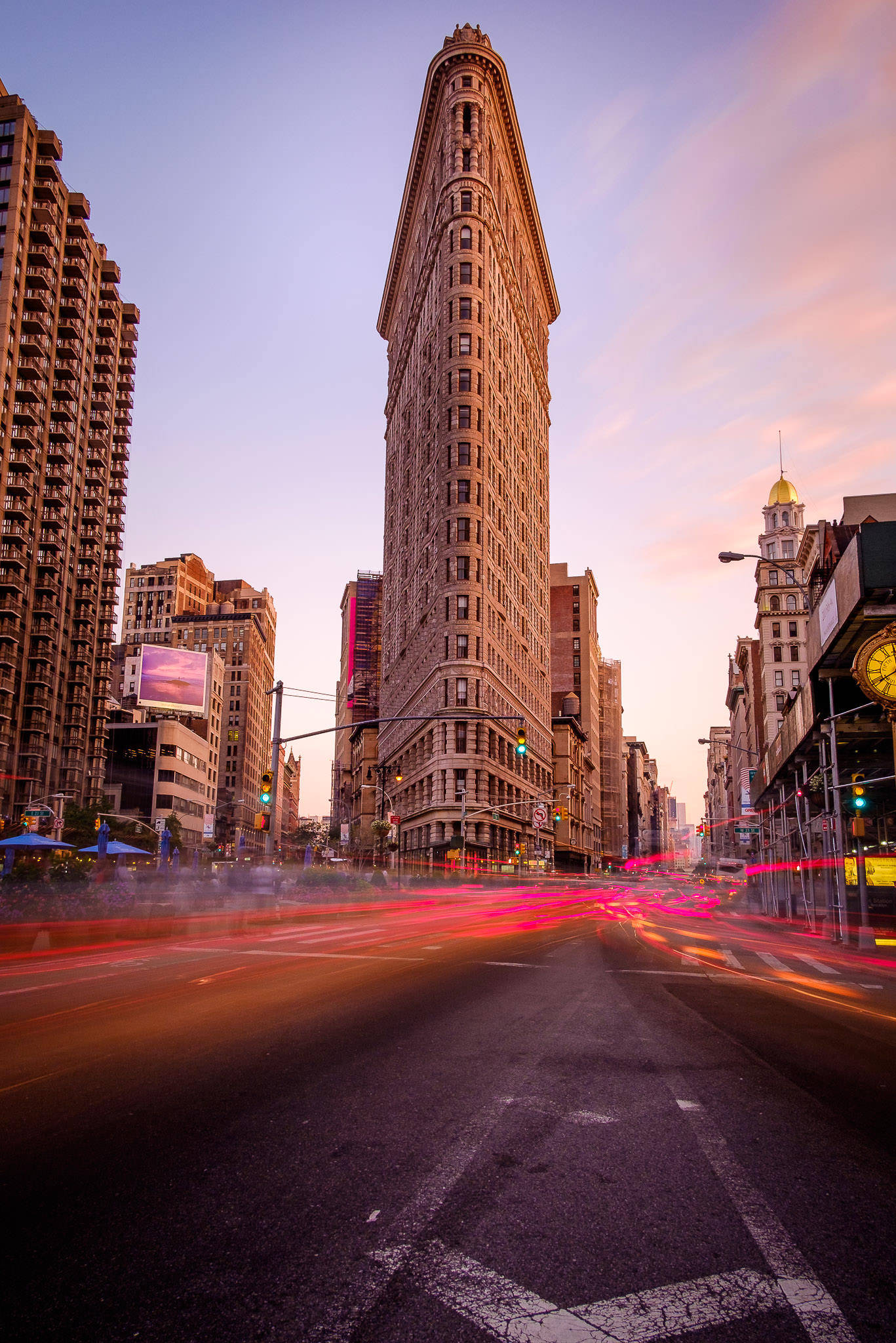 Flatiron Building 桌布 壁紙 — 熨斗大廈在紐約市高聳矗立，黃昏時分，紅色和橙色的光線條紋模糊地掠過街道。