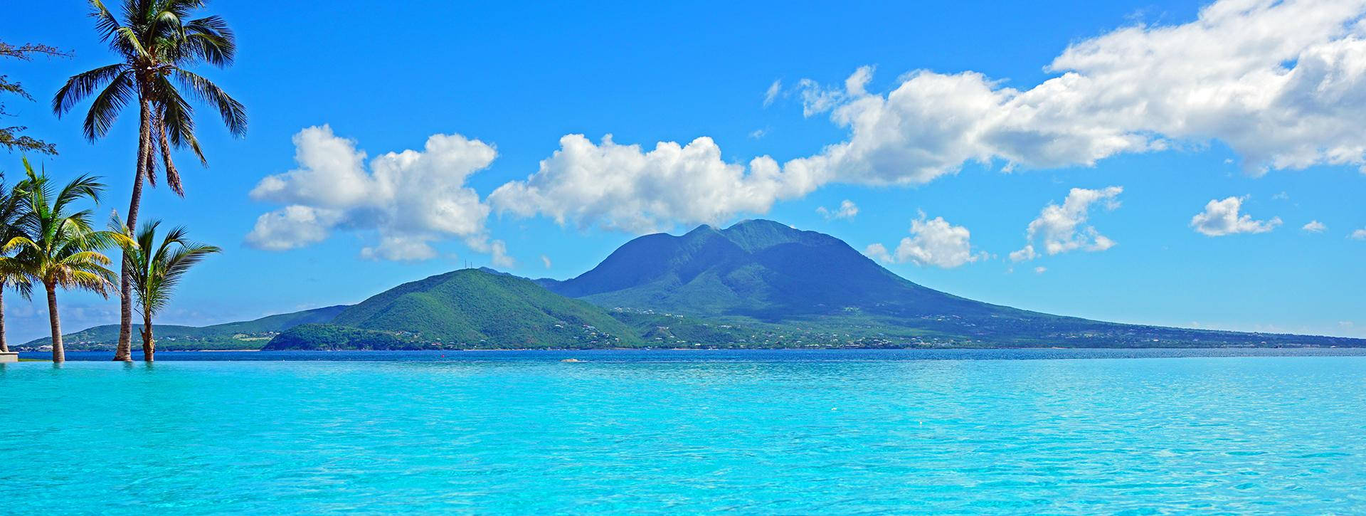 島嶼 桌布 壁紙 — 熱帶天堂，有碧綠海水、棕櫚樹和鬱鬱蔥蔥的綠色山脈，在明亮的藍天和蓬鬆的白雲下。