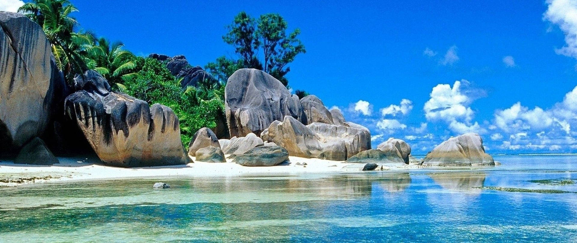 熱帶海灘，有巨石和棕櫚樹，在明亮的藍天下。 — 2560x1080 動態桌布 壁紙