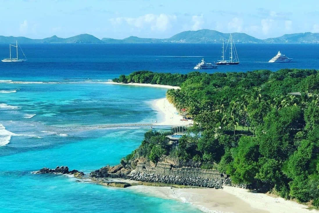 Caribbean Island 桌布 壁紙 — 熱帶天堂的鳥瞰圖，有碧綠的海水、白色沙灘、茂密的綠色山丘和停泊在近海的豪華遊艇。