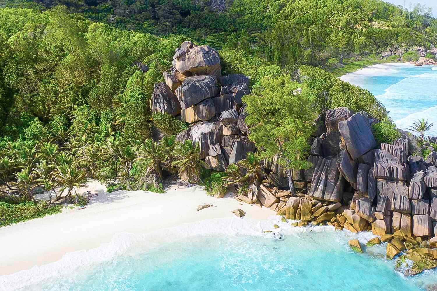 Bora Bora Beach 桌布 壁紙 — 熱帶天堂的鳥瞰圖，碧綠的海水拍打著白色沙灘和巨大的花崗岩巨石，周圍環繞著茂密的綠色叢林。