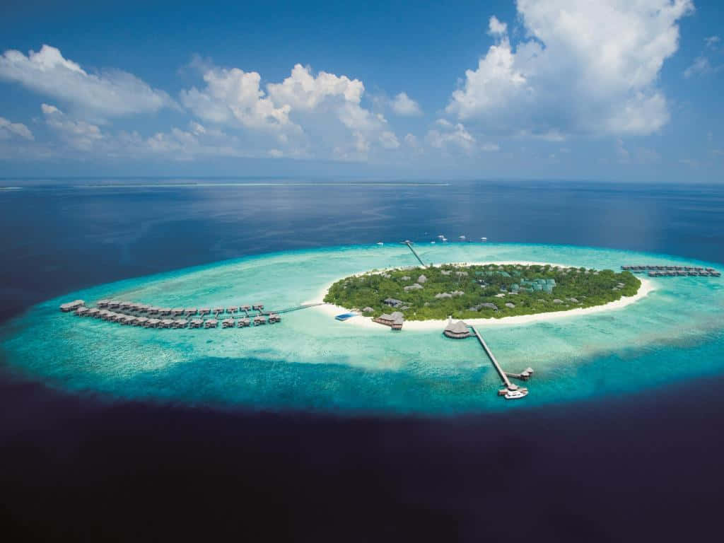 Maldives Island 桌布 壁紙 — 熱帶島嶼度假村的鳥瞰圖，擁有水上平房和碧綠色的潟湖，在明亮的藍天和白雲下。