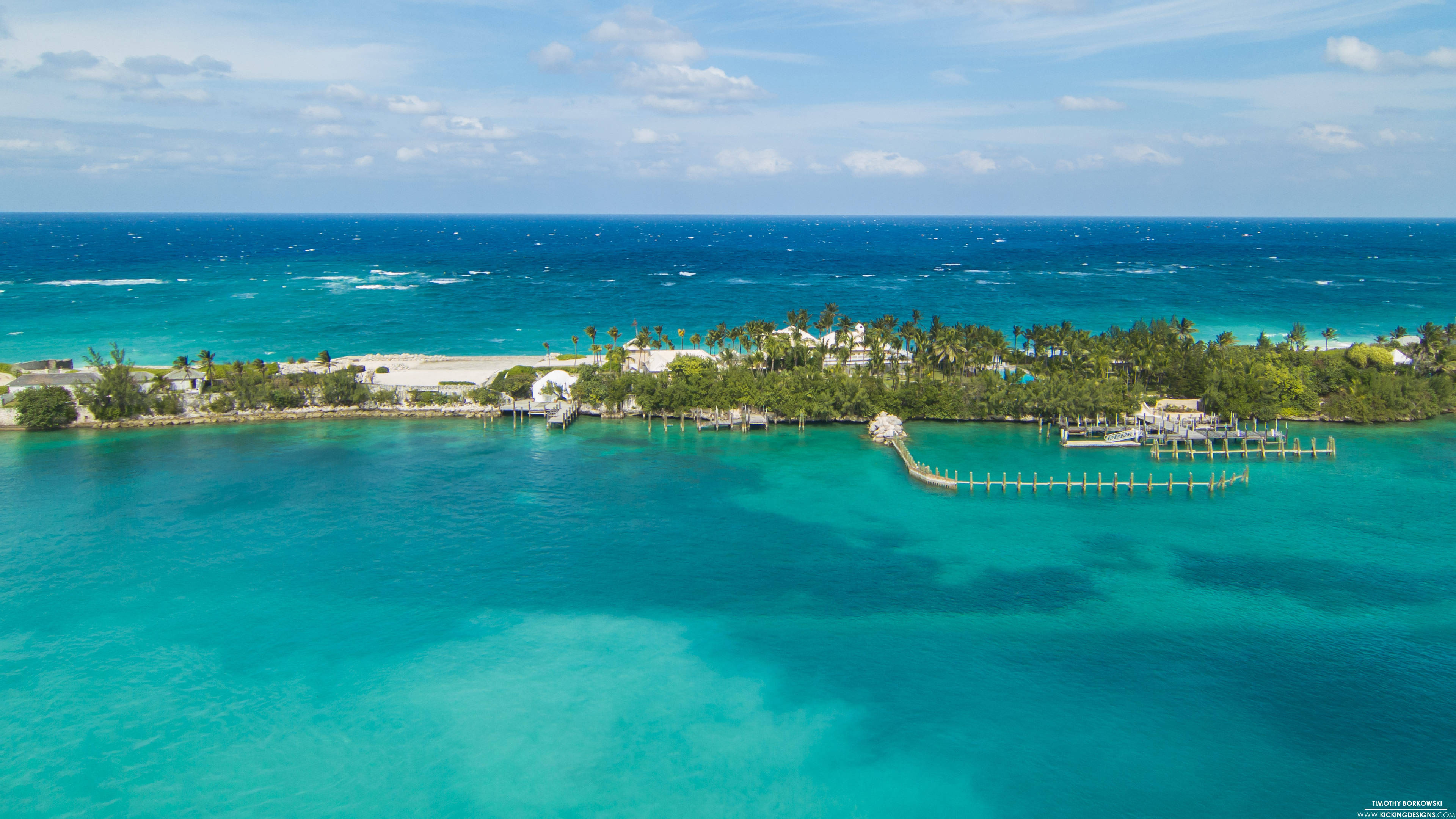 Nassau Bahamas 桌布 壁紙 — 熱帶島嶼的鳥瞰圖，擁有碧綠海水、棕櫚樹和木製碼頭，在明亮的藍天下。