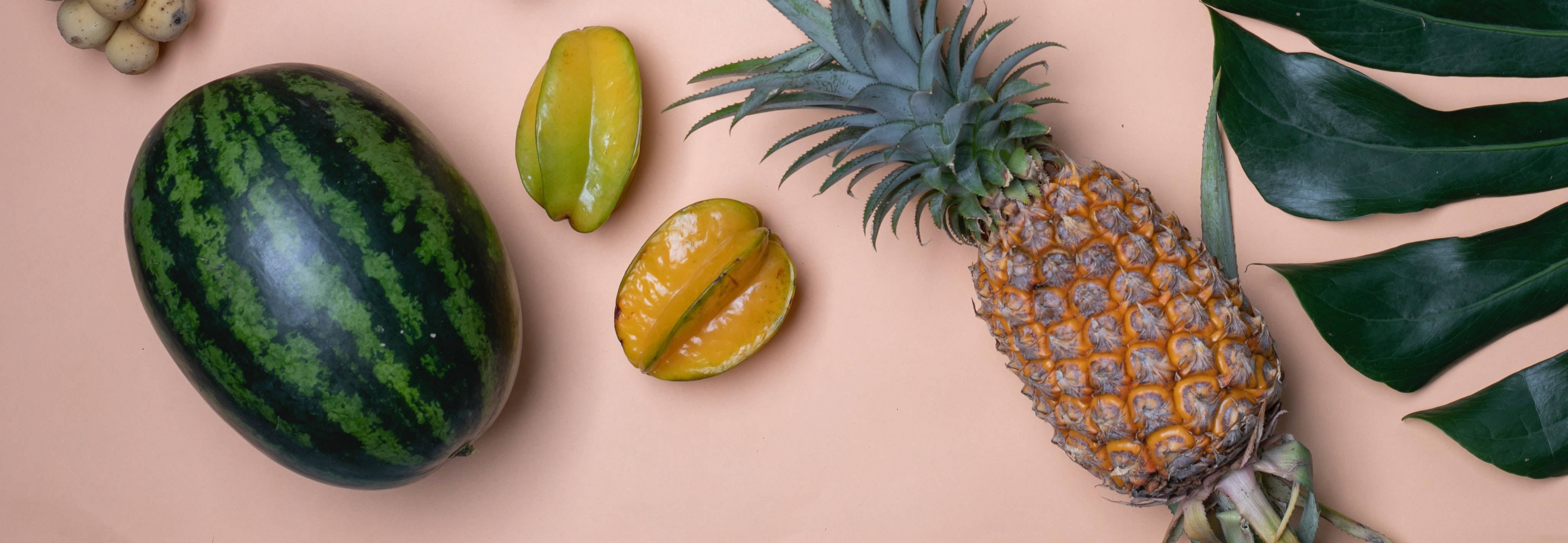Fruit 桌布 壁紙 — 熱帶水果包括西瓜、鳳梨和楊桃，搭配龜背竹葉，排列在柔和的蜜桃色背景上。