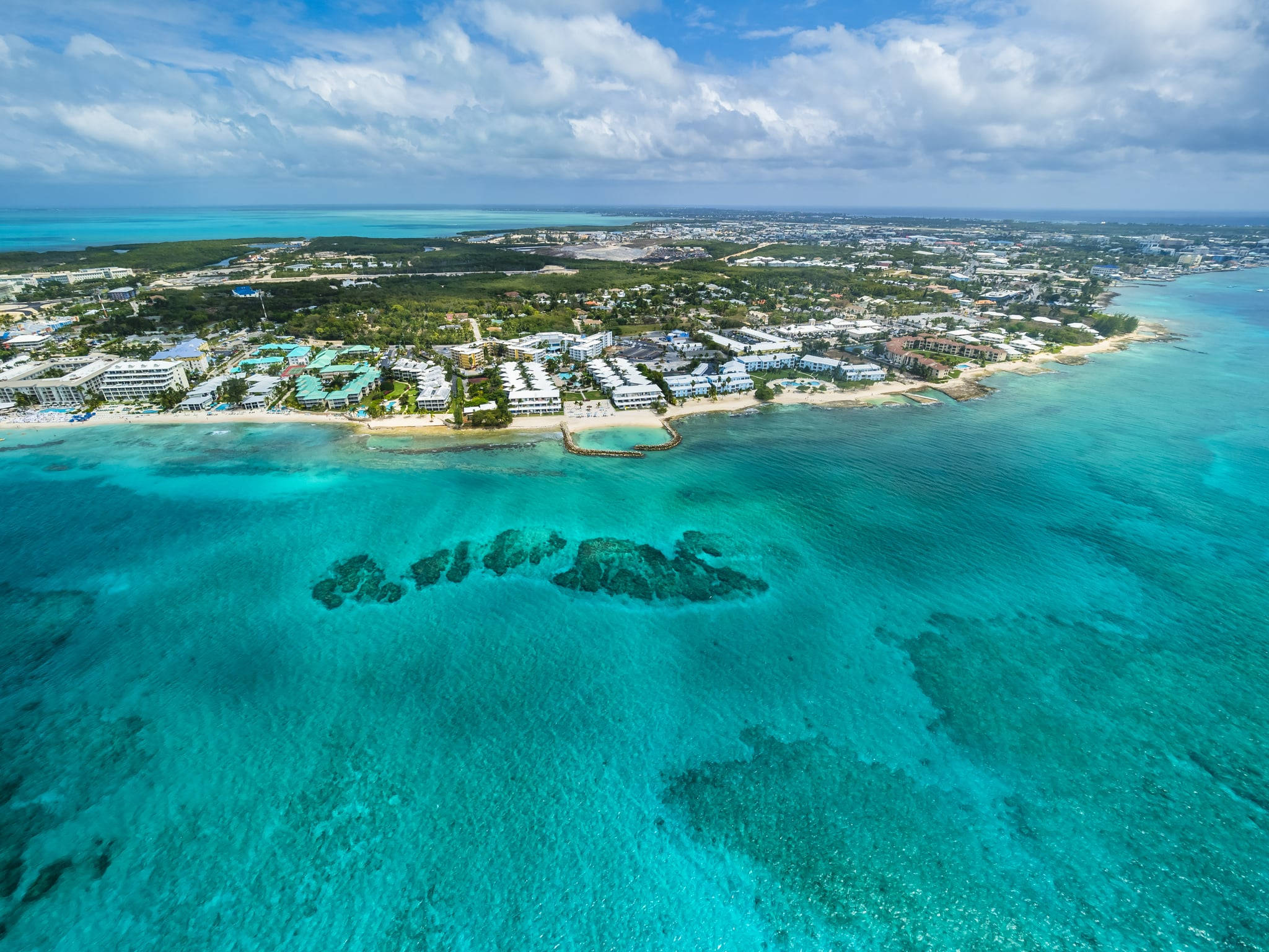 Cayman 桌布 壁紙 — 熱帶沿海小鎮的鳥瞰圖，擁有碧綠的海水和白色沙灘，天空部分多雲。