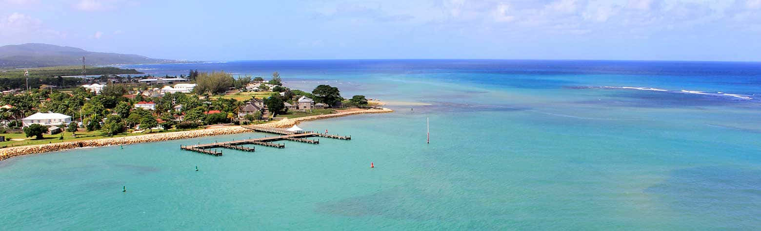 Jamaican Island 桌布 壁紙 — 熱帶海岸線的鳥瞰圖，有碧綠的海水、溫柔的海浪和一個隱藏在綠樹中的小沿海村莊。