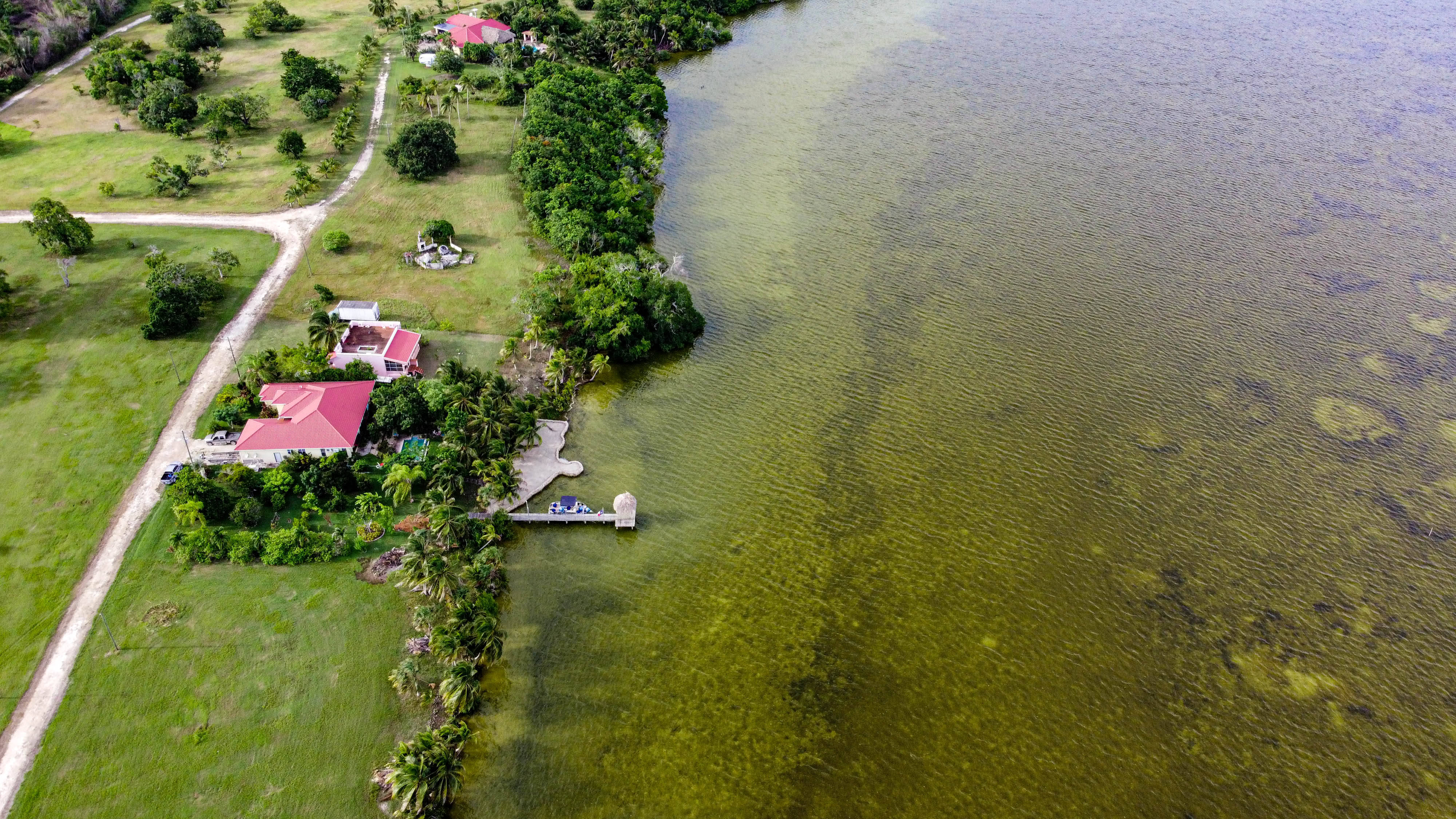 Belize 桌布 壁紙 — 熱帶海濱物業的鳥瞰圖，紅色屋頂的房子停泊在清澈的綠色水域中，周圍環繞著茂密的綠植。