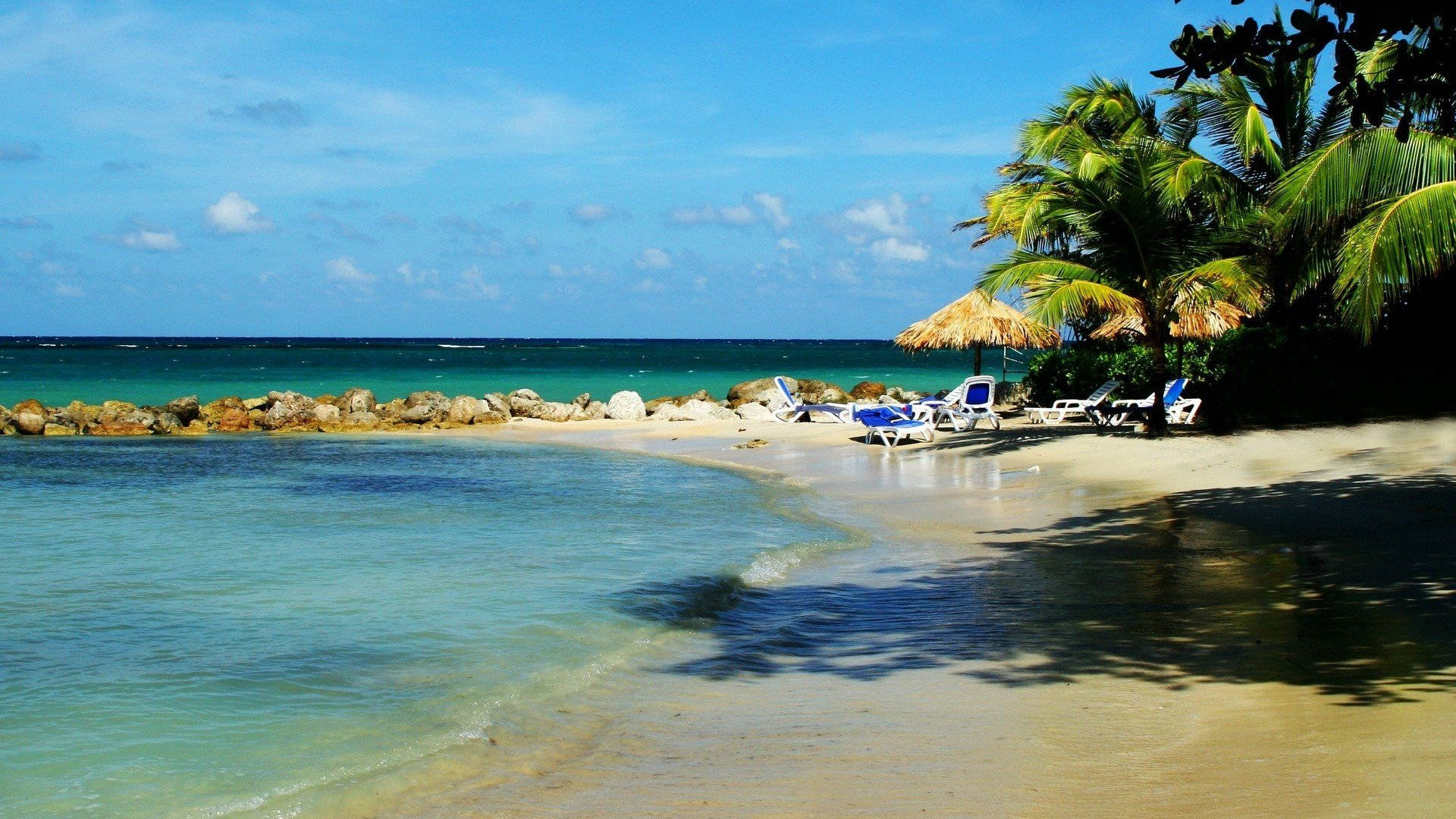 Jamaica 桌布 壁紙 — 熱帶海灘，有碧綠海水、棕櫚樹和躺椅，在明亮的藍天下。