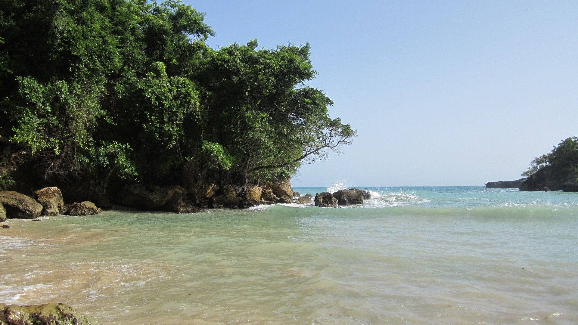 Haiti 桌布 壁紙 — 熱帶海灘，碧綠的海水拍打著沙灘，四周是茂密的綠色叢林懸崖，頭頂是清澈的藍天。