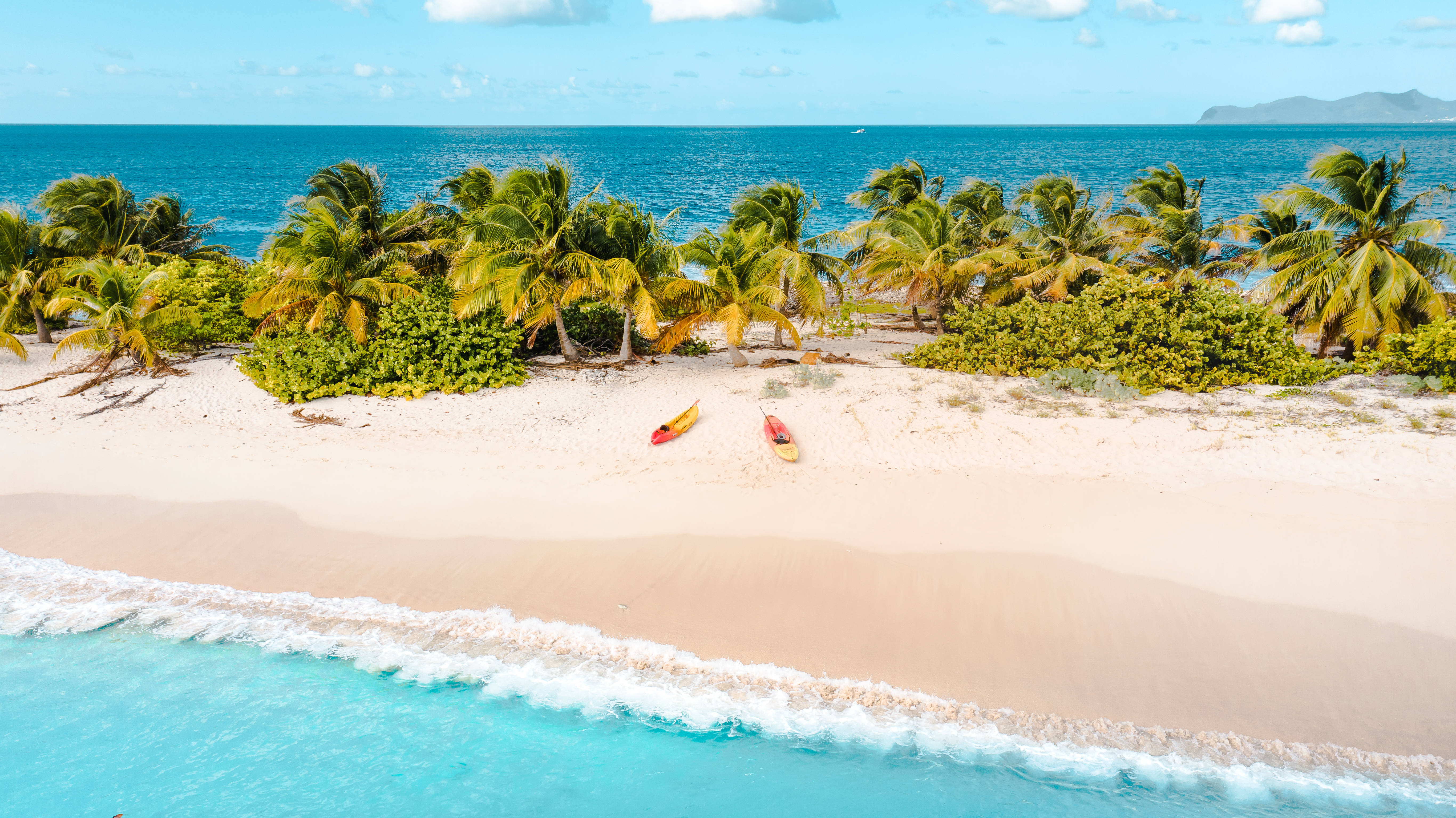 Grenada 桌布 壁紙 — 熱帶海灘的鳥瞰圖，有碧綠的海水、溫柔的海浪、白色的沙灘，以及兩艘在搖曳的棕櫚樹下休息的皮划艇。
