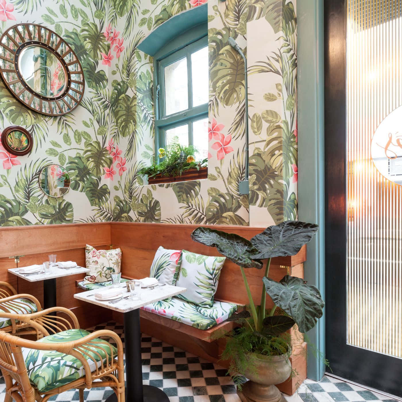 Restaurant 桌布 壁紙 — 熱帶風格壁紙，粉紅花朵與綠葉點綴著舒適的餐廳角落，配有木製卡座、藤椅和格子地板。