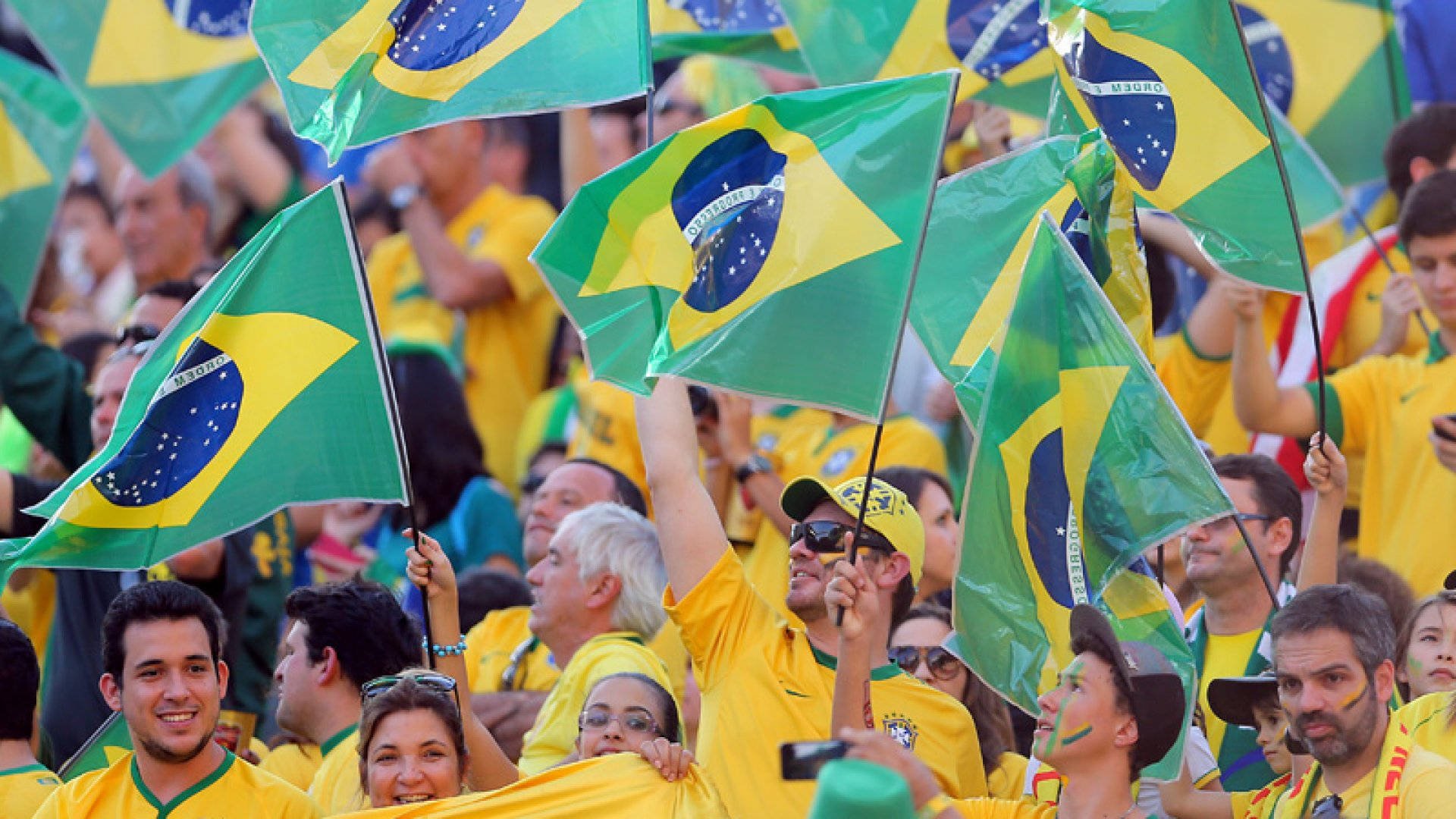 Brazil Flag 桌布 壁紙 — 熱情的巴西球迷在日間體育賽事中，於擠滿人的體育場揮舞綠色黃色旗幟。