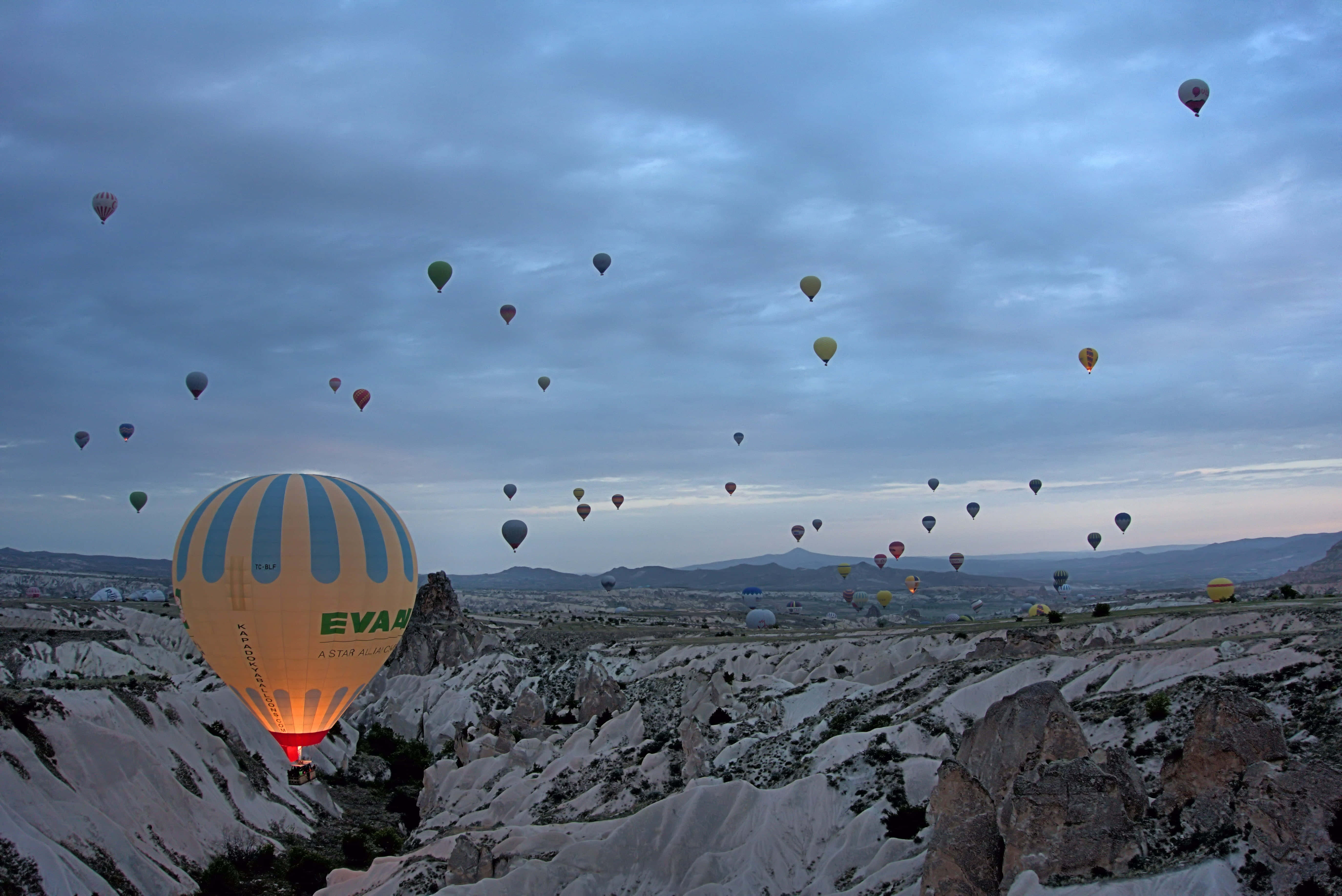 Hot Air Balloon 桌布 壁紙 — 熱氣球在卡帕多奇亞崎嶇的岩石地貌上，於暮色天空中溫暖地發光。