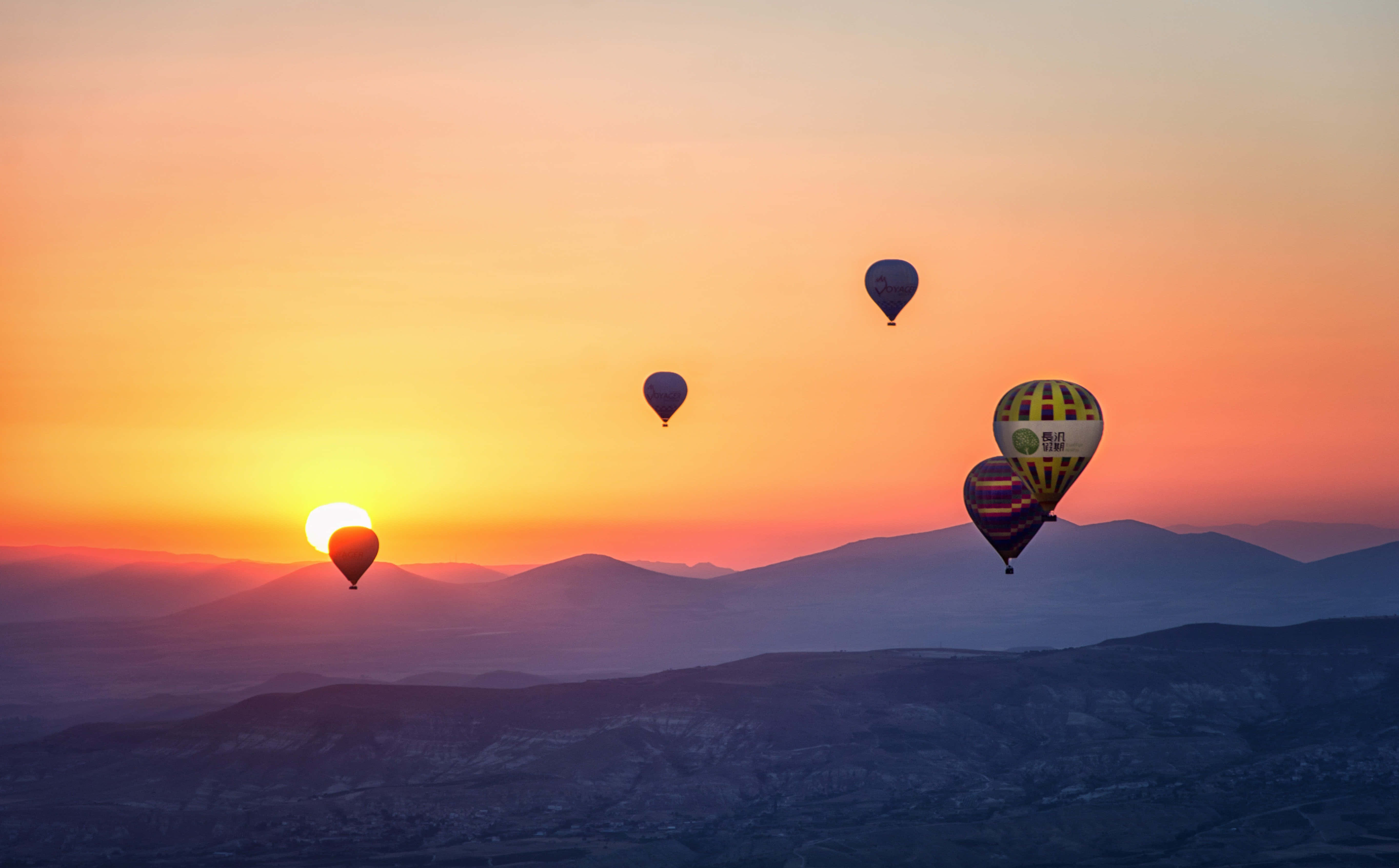 Balloon 桌布 壁紙 — 熱氣球在山脈上空飄移，太陽以火熱的橙色和粉紅色調升起。