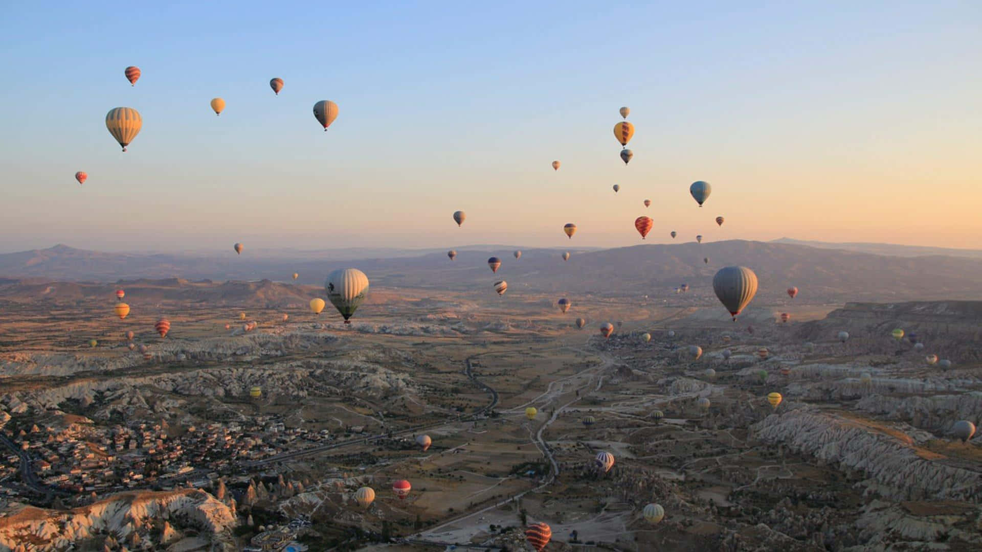 Hot Air Balloon 桌布 壁紙 — 熱氣球在日出時分飄過崎嶇的山谷，將溫暖的光線灑落在風景上。