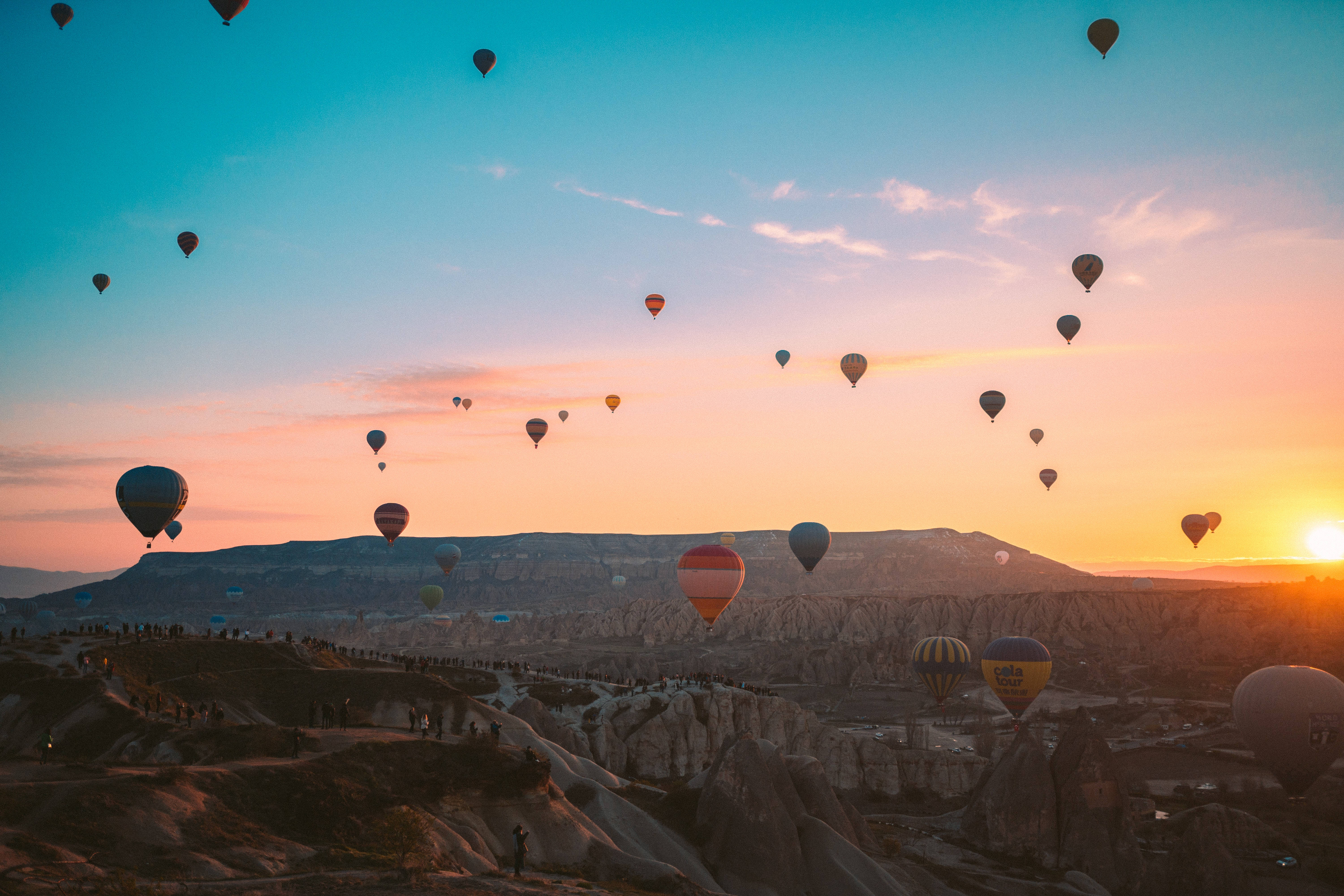 Cappadocia 桌布 壁紙 — 熱氣球在日出時分飄過崎嶇的火山地形，在天空中投下溫暖的色調。
