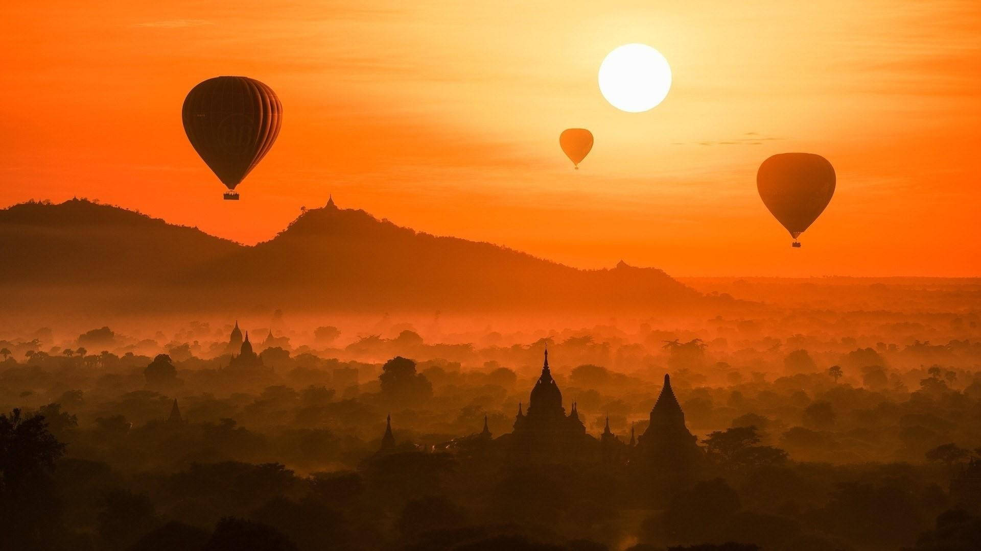 Yangon 桌布 壁紙 — 熱氣球在日出時飄過煙霧繚繞的寺廟，為整個景觀投射出溫暖的橙色光芒。