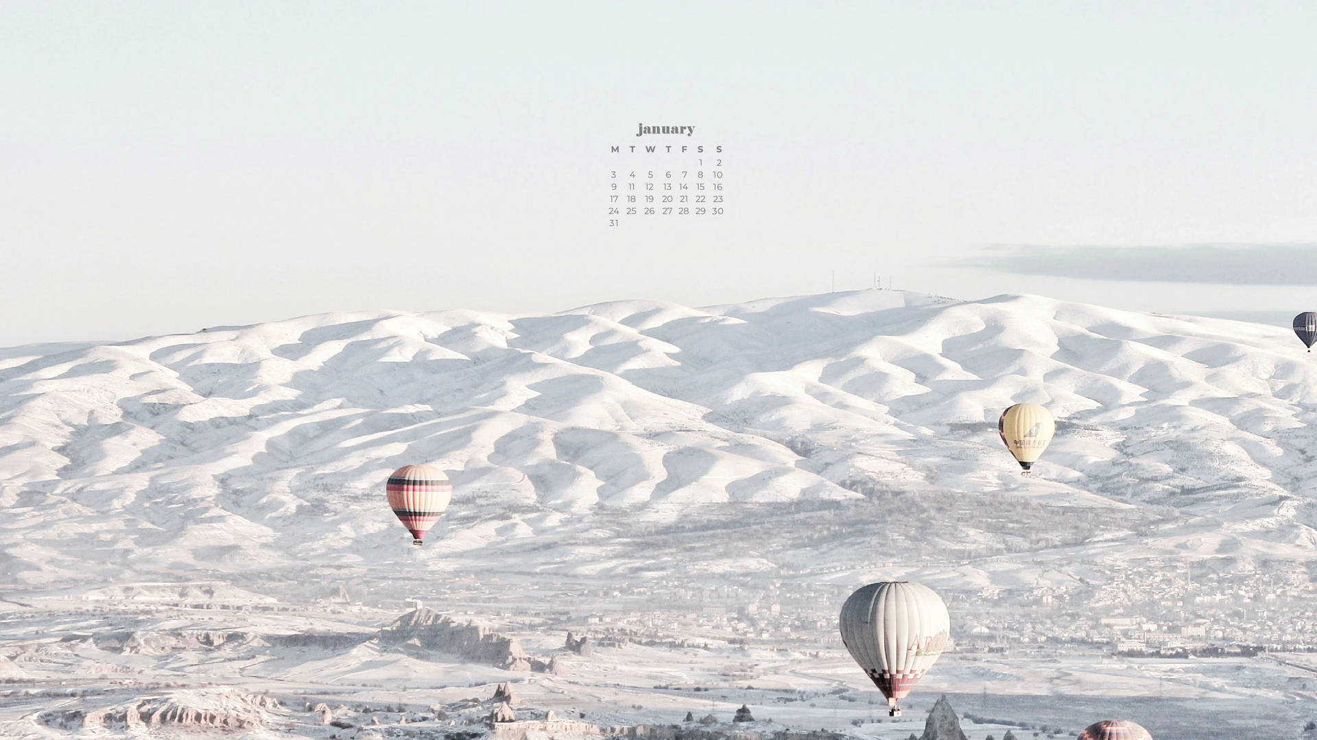 熱氣球漂浮在雪丘上空，天空有一月日曆。 — 一月 GIF 壁紙