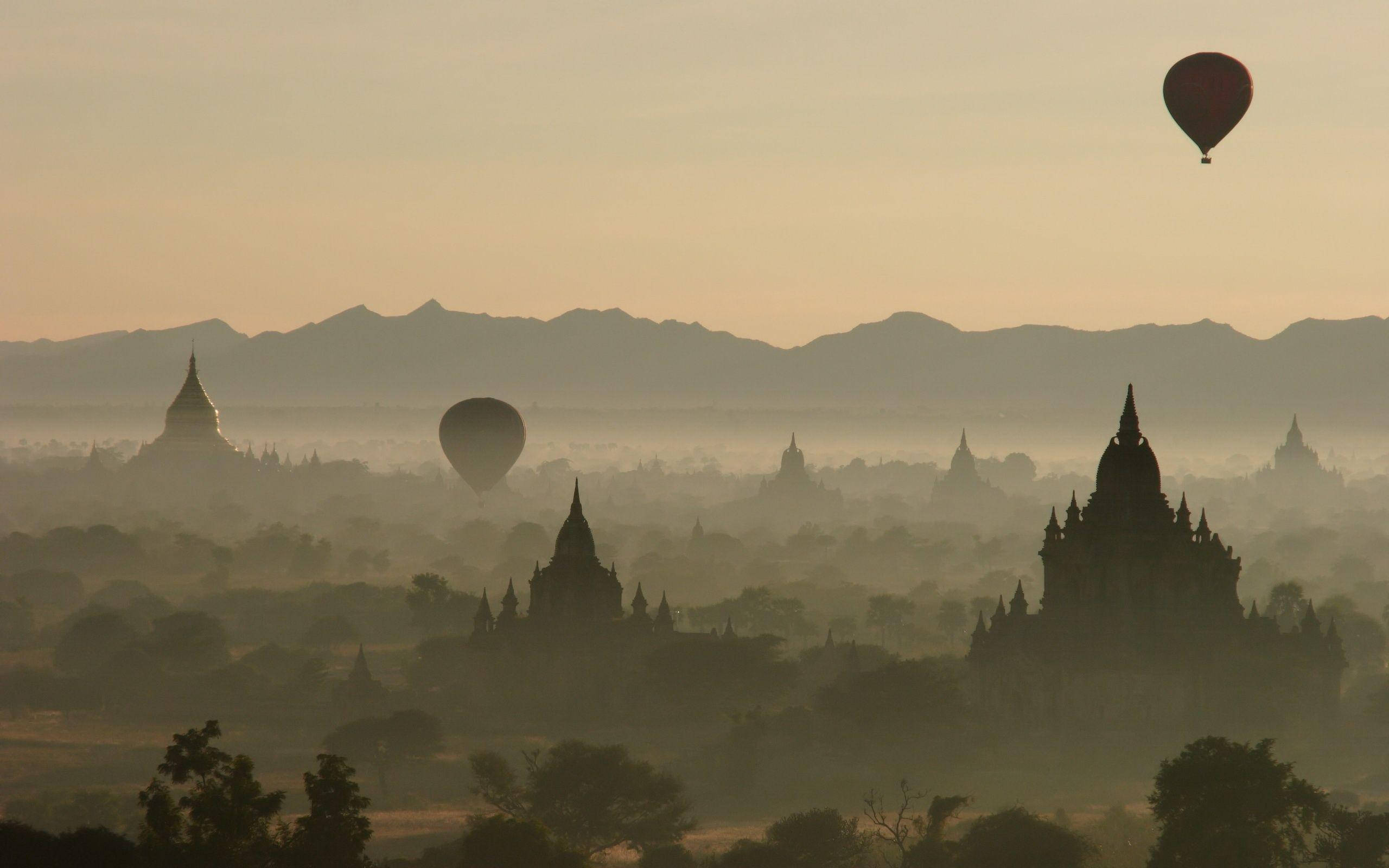 Burma 桌布 壁紙 — 熱氣球在蒲甘黎明時分飄過霧氣籠罩的古老寺廟，伴隨著柔和的金色光芒。