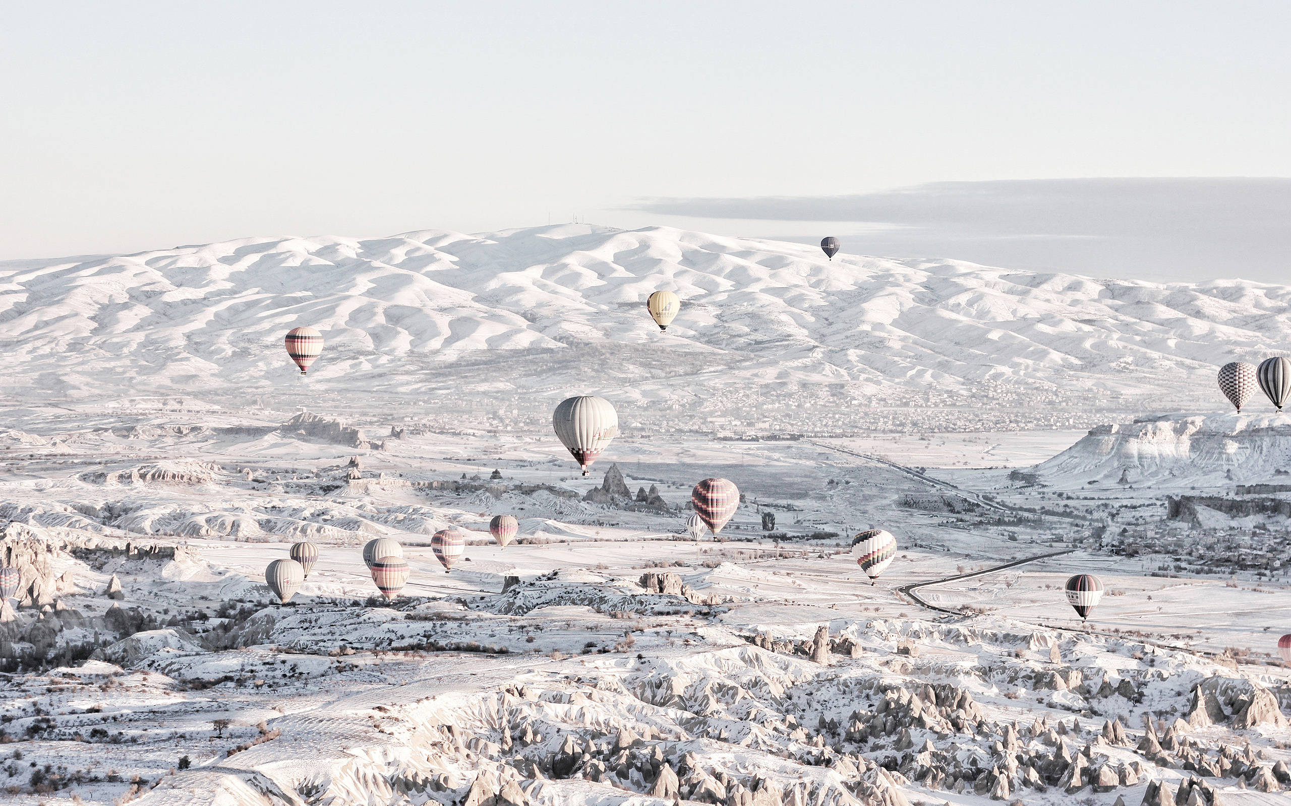 Cappadocia 桌布 壁紙 — 熱氣球在蒼白的天空下飄過白雪覆蓋的火山景觀。