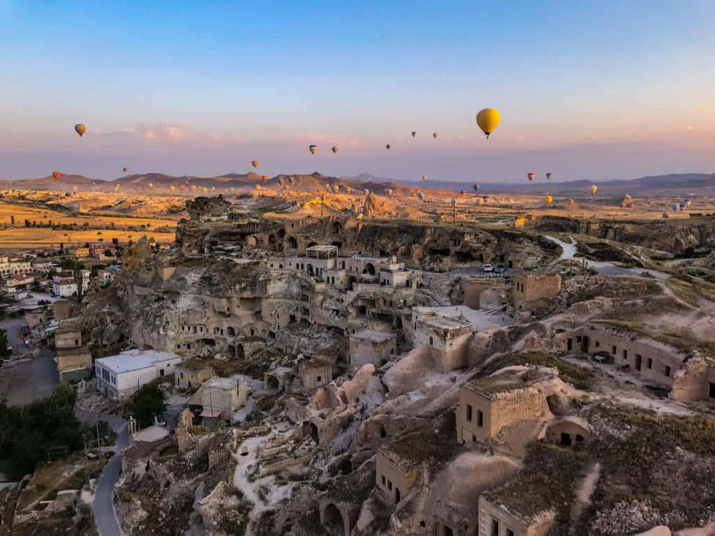 Hot Air Balloon 桌布 壁紙 — 熱氣球在金色日落時分飄過卡帕多奇亞的古老洞穴住宅。