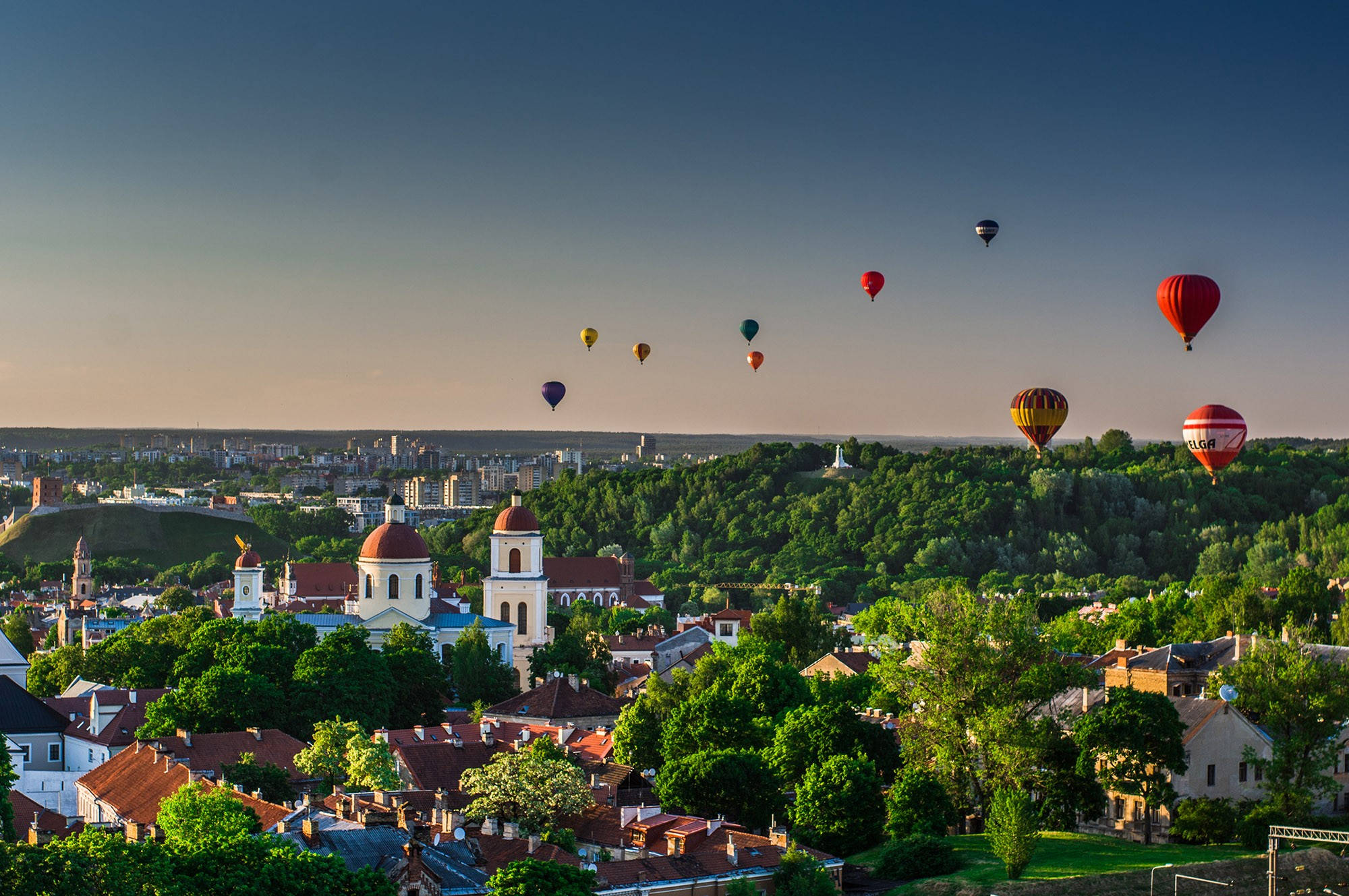 Vilnius 桌布 壁紙 — 熱氣球在金色日落時分飄過翠綠的山坡和歷史小鎮。