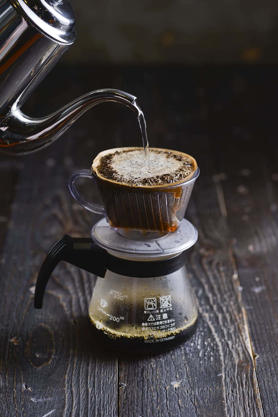Coffee Aesthetic 桌布 壁紙 — 熱水從鵝頸壺倒入玻璃咖啡滴濾器，置於深色木桌上。