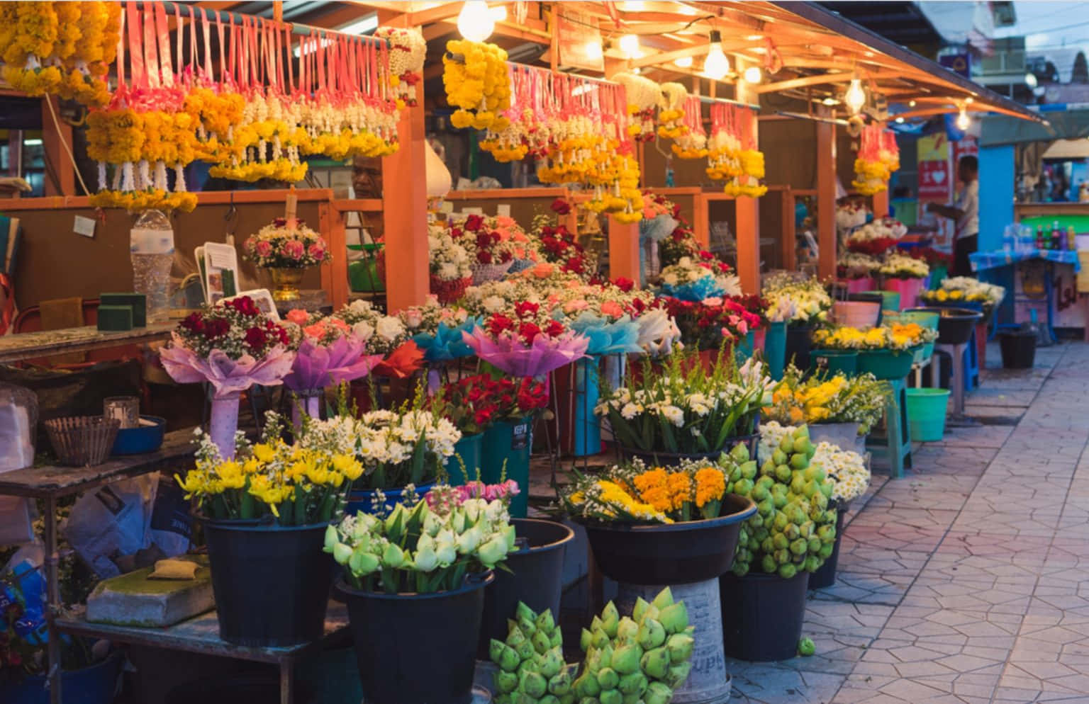 Flower Market 桌布 壁紙 — 熱鬧的夜市裡，色彩繽紛的花攤排列整齊，掛著花環和鮮花，在溫暖的燈光下。